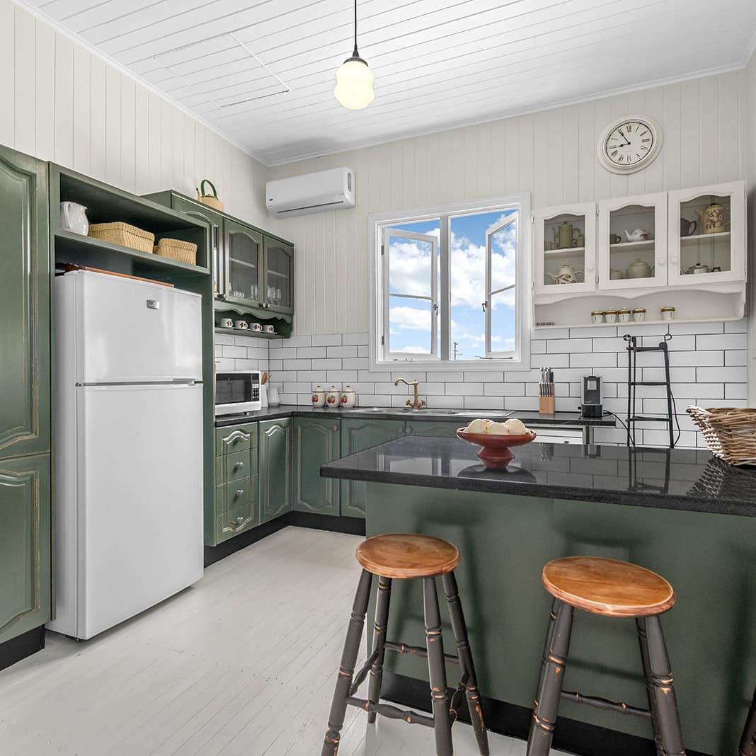 Spacious kitchen with dark green cabinets, white tile backsplash, black granite countertops, and an island with bar stools.