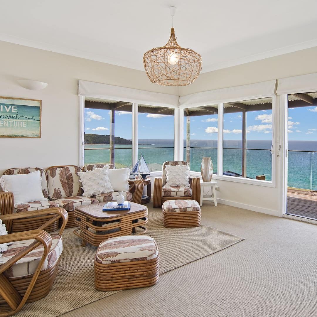 Open living room of an oceanfront home with rattan sofas and chairs, carpeted floors, lots of windows, and a balcony.