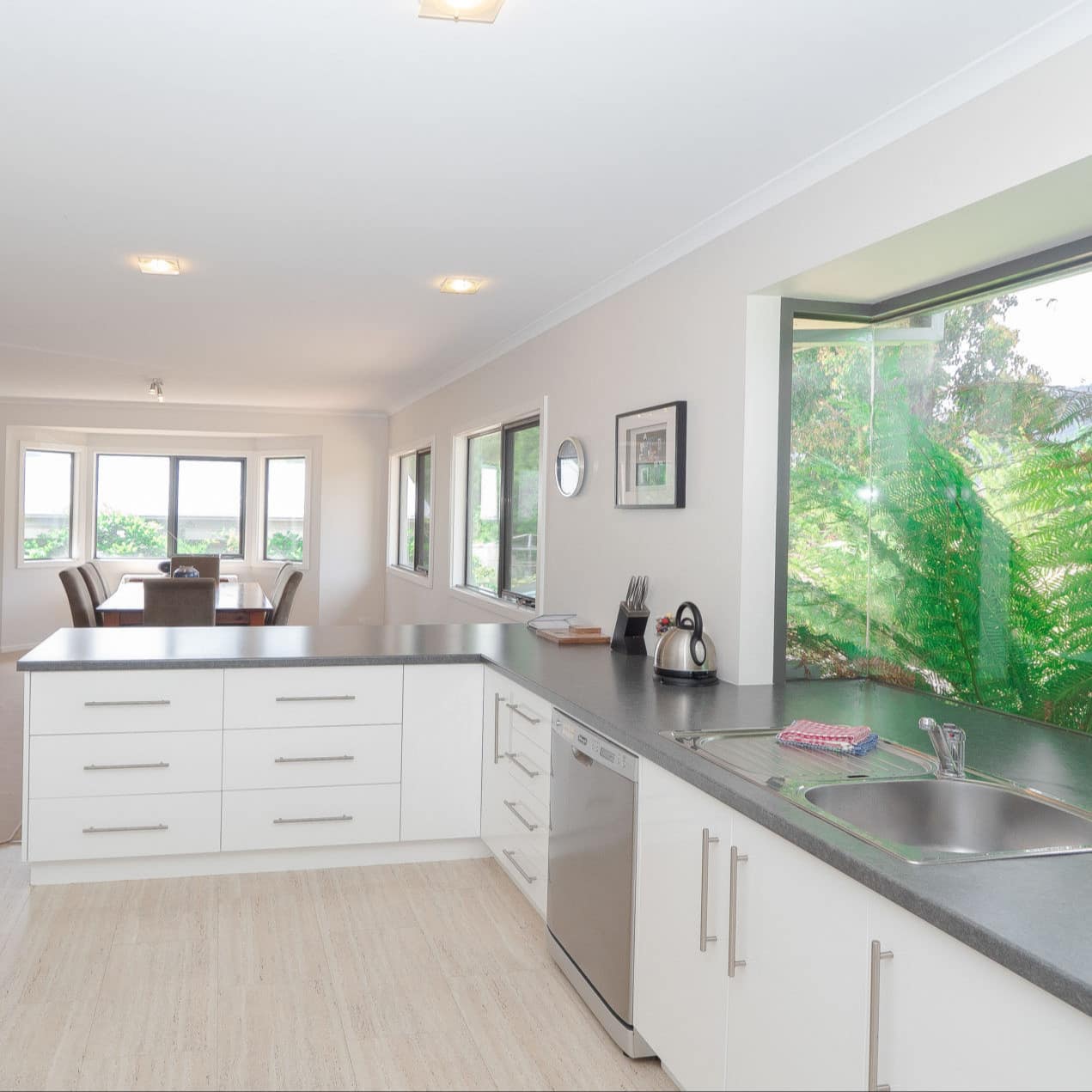 Spacious, modern kitchen with white cabinets, grey countertops, and a wide window with views of tropical plants.