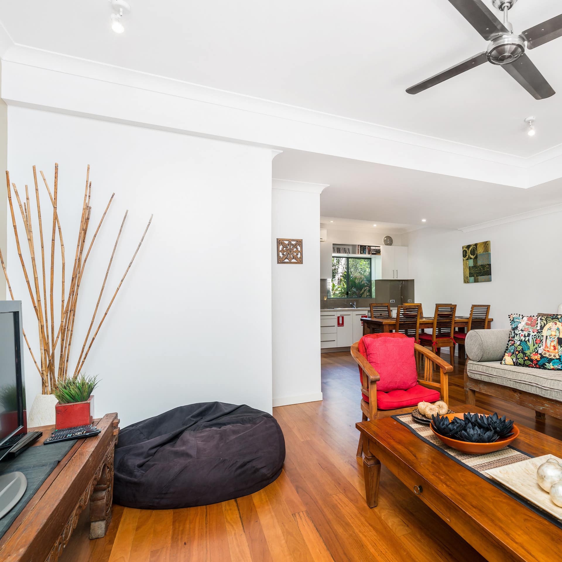 Open living room with hardwood floors, white walls, wooden furniture, flatscreen TV and red and grey decor.