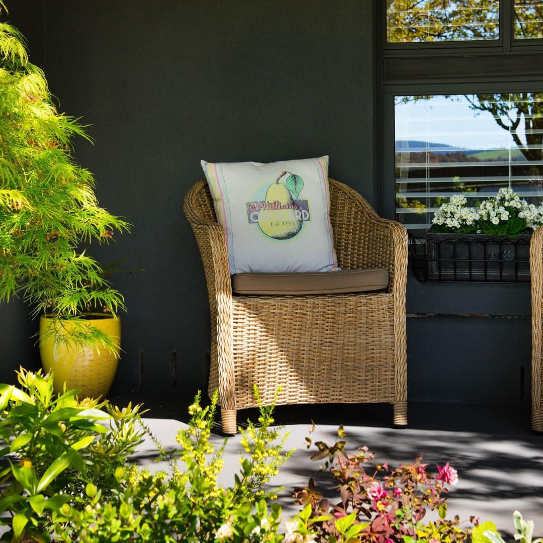Sunny porch with two wicker chairs and lush greenery.