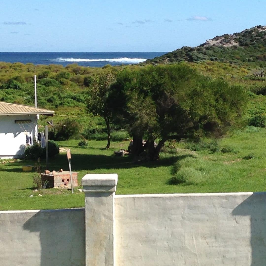 The view from the verandah of a beach house with green, lush hillsides and the ocean with crashing waves in the background.