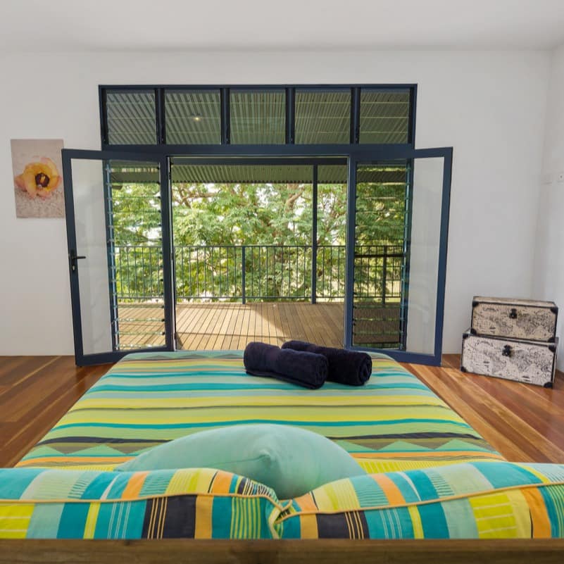 Open bedroom with hardwood floors, white walls, king-size bed, green and blue bedding, glass doors to a covered patio.