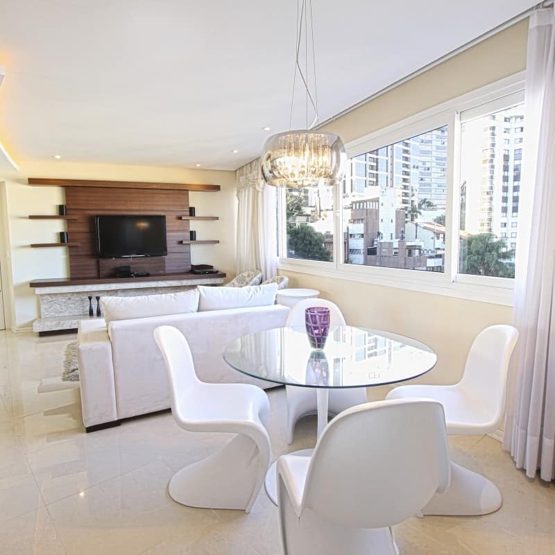 Modern apartment with open living and dining room, glass table with white fiberglass chairs, a white sofa and stone floor