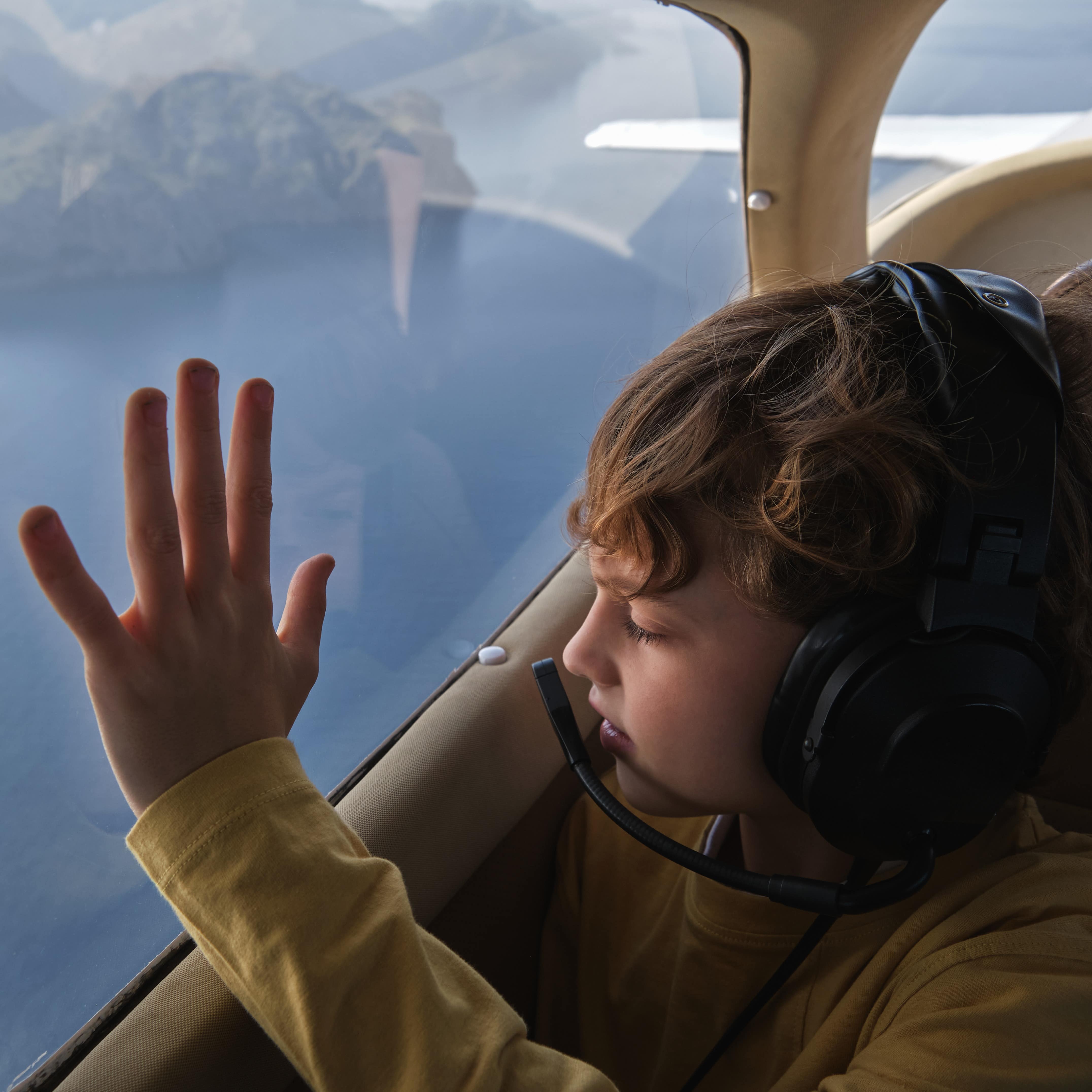 Young boy with hand on private plane window looking down on islands at sea