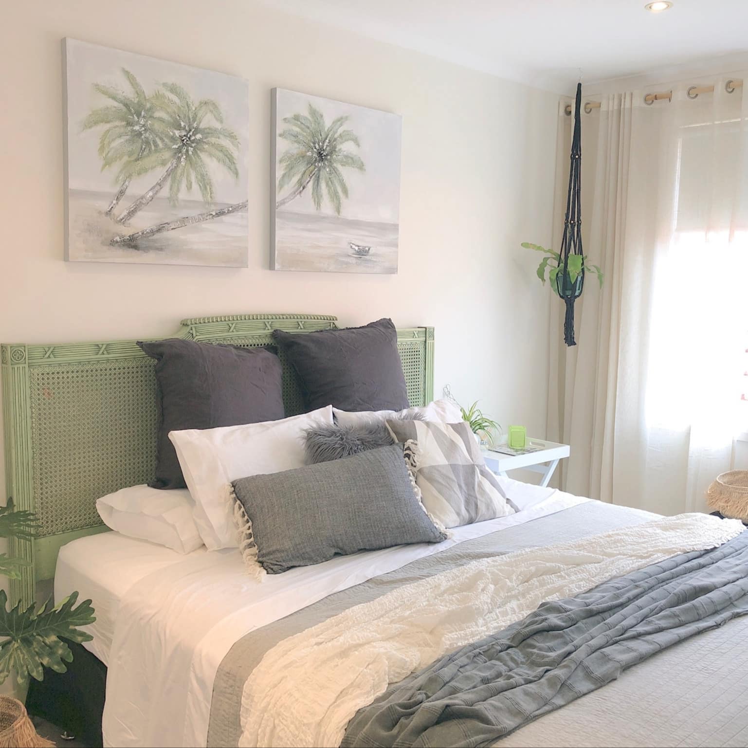 Tropical-inspired bedroom with a king size bed with grey and white bedding and a light green wicker headboard.