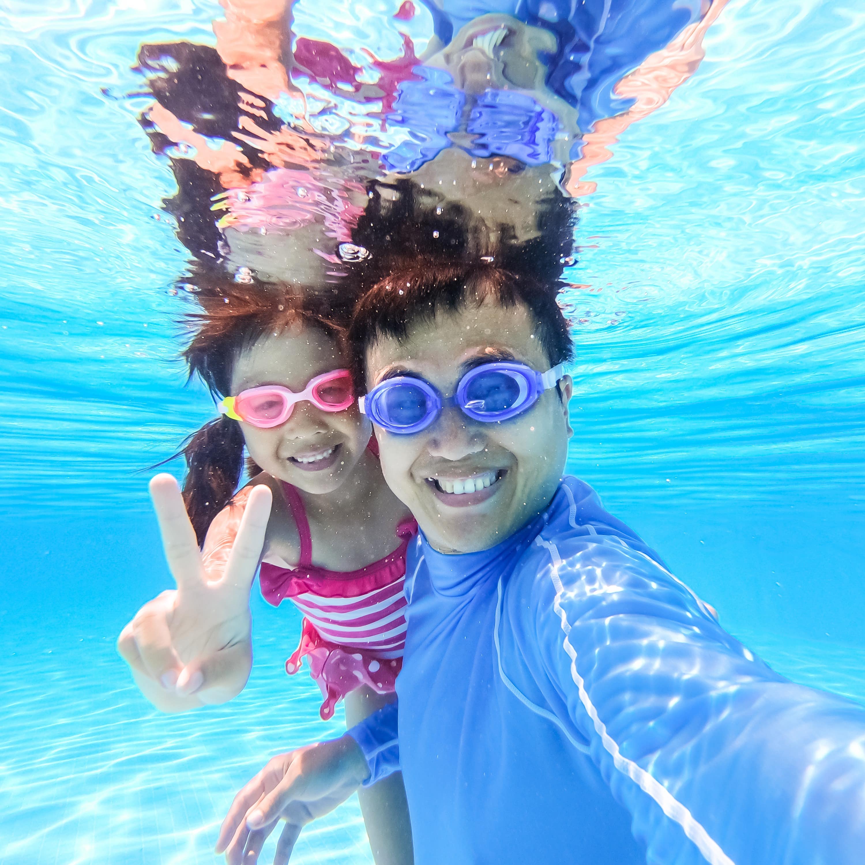 Dad and daughter underwater in a pool 