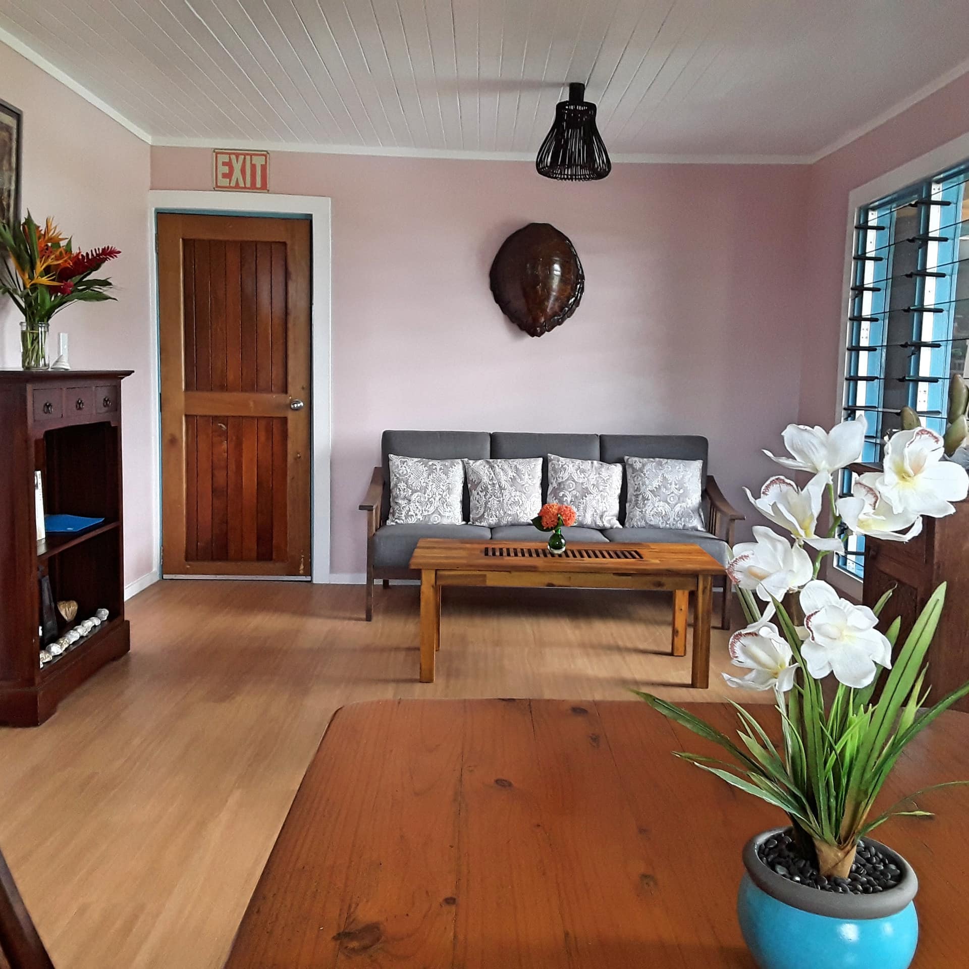 Open living and dining room with hardwood floors, light pink walls, a wooden dining set and a grey sofa.