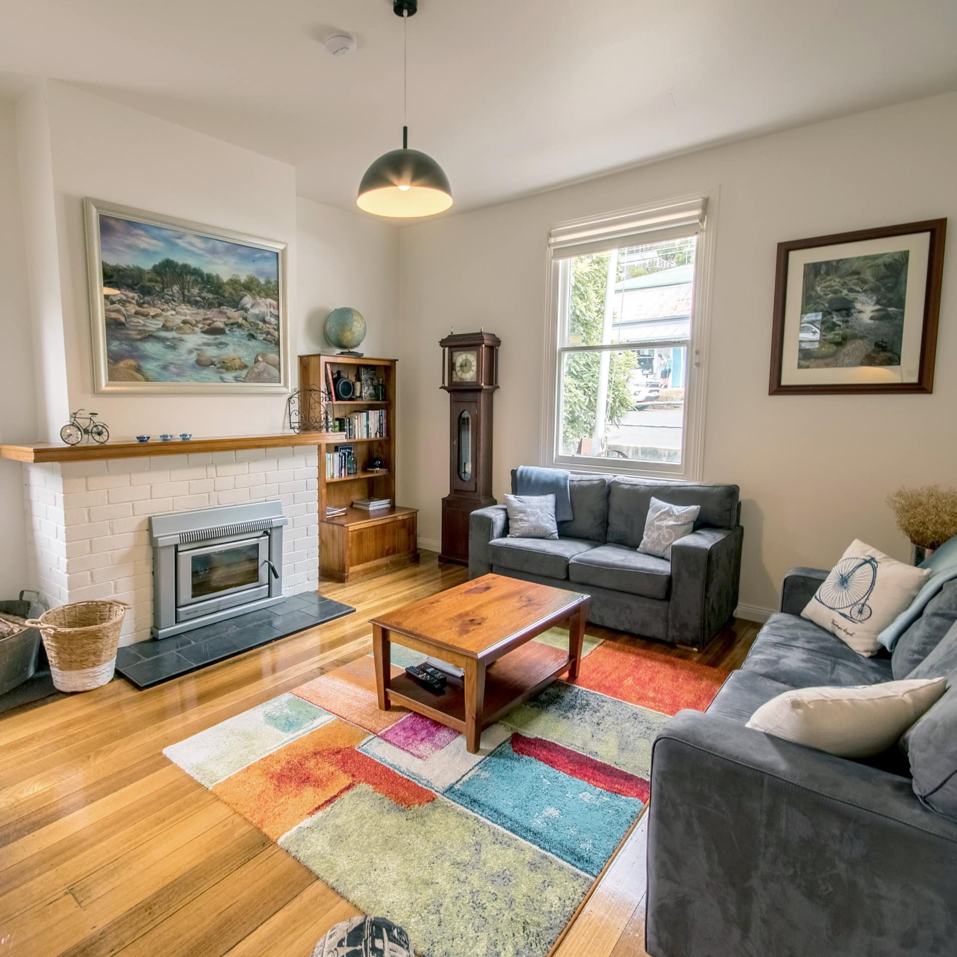 Living room of 4-bedroom lodge with hardwood floors, blue cloth sofa and love seat, colourful rug and central fireplace