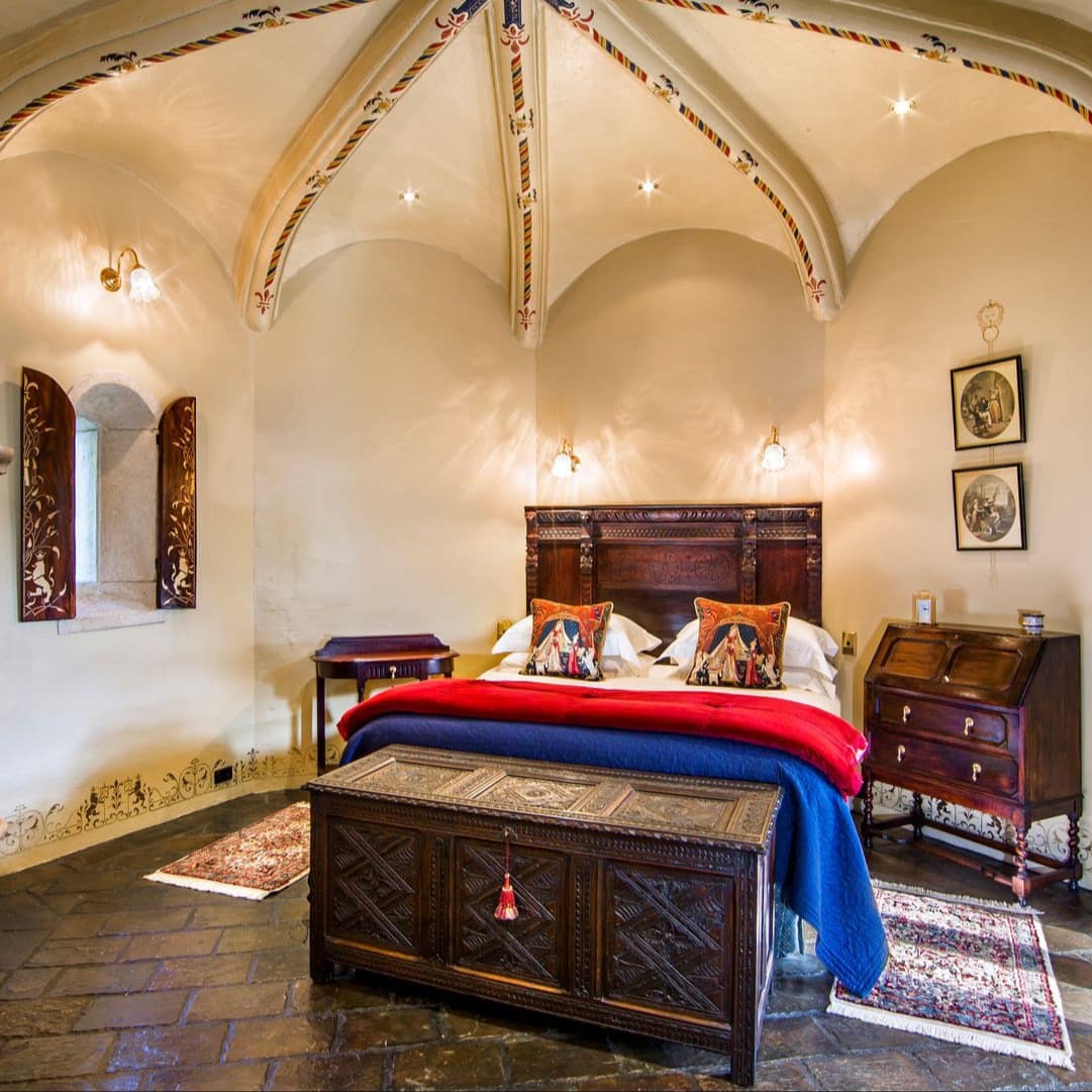 Romantic castle B & B bedroom with massive carved stone fireplace, decorated, arched ceiling and arched, windowed doorway