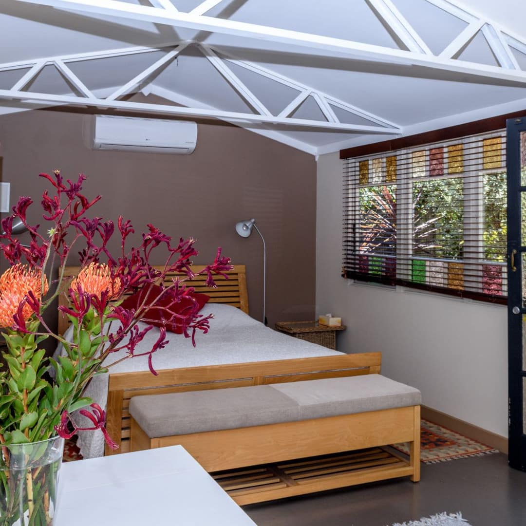 Bedroom of Studio 44 B & B with a wood bed and bench, wicker chair, stained-glass windows and private garden entrance.