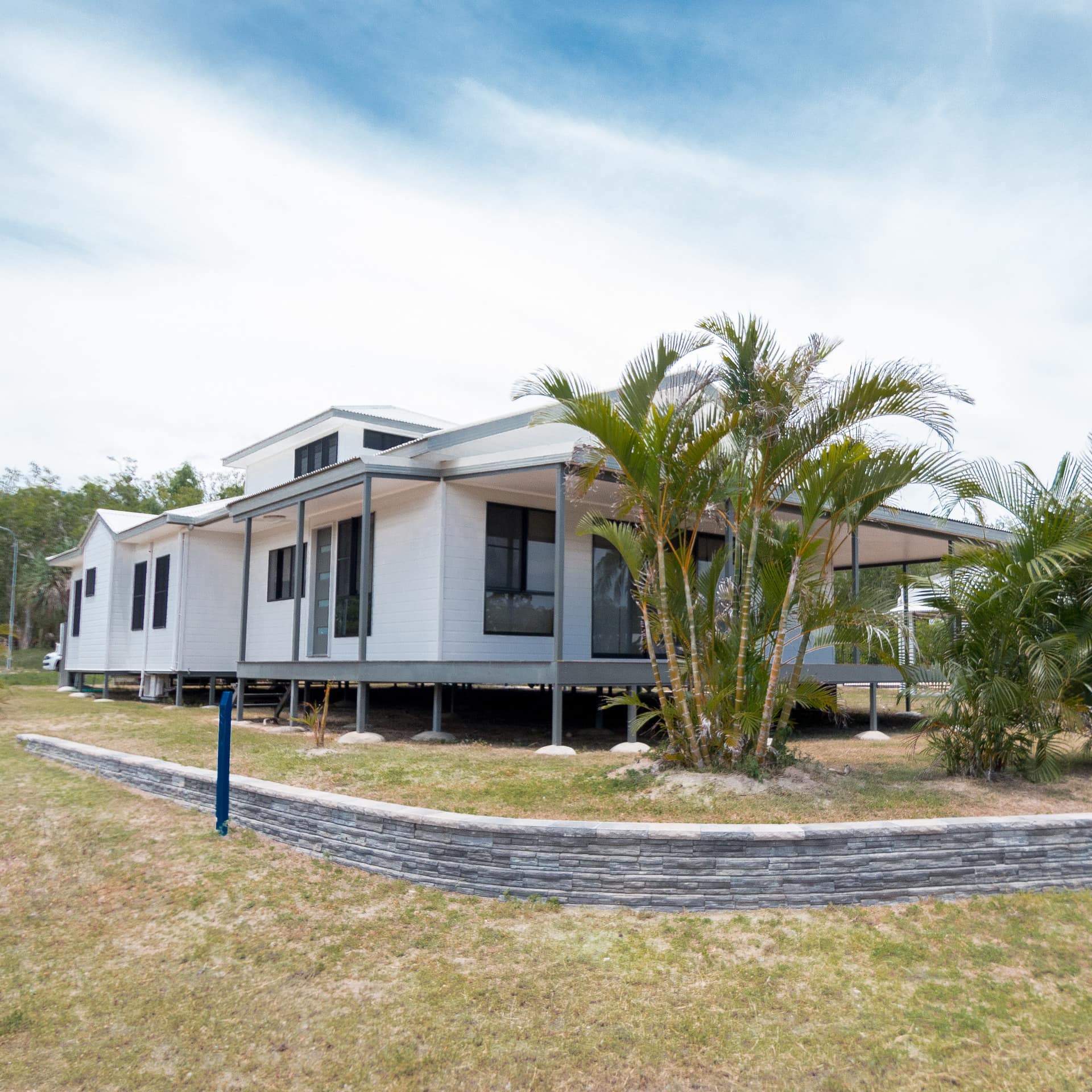 White ranch-style home with covered deck and landscaped lawn with tropical plants.