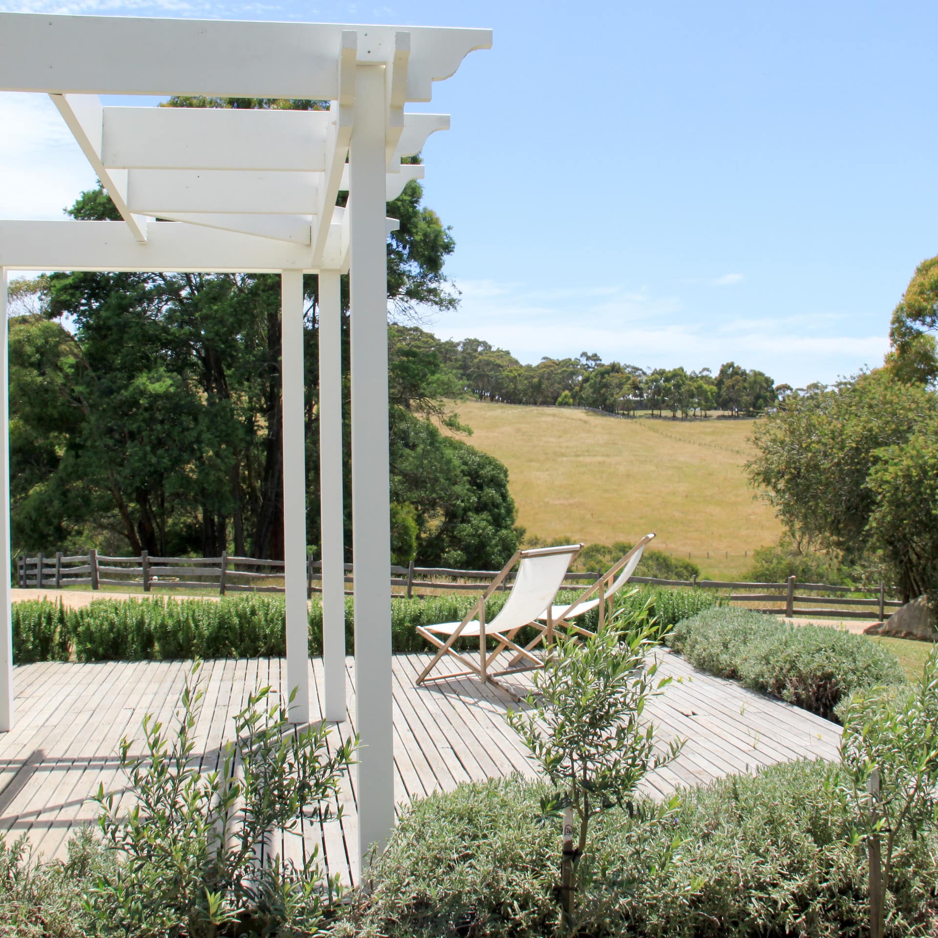 Two canvas lounge chairs on wooden deck with white pavilion overlooking rural landscape.