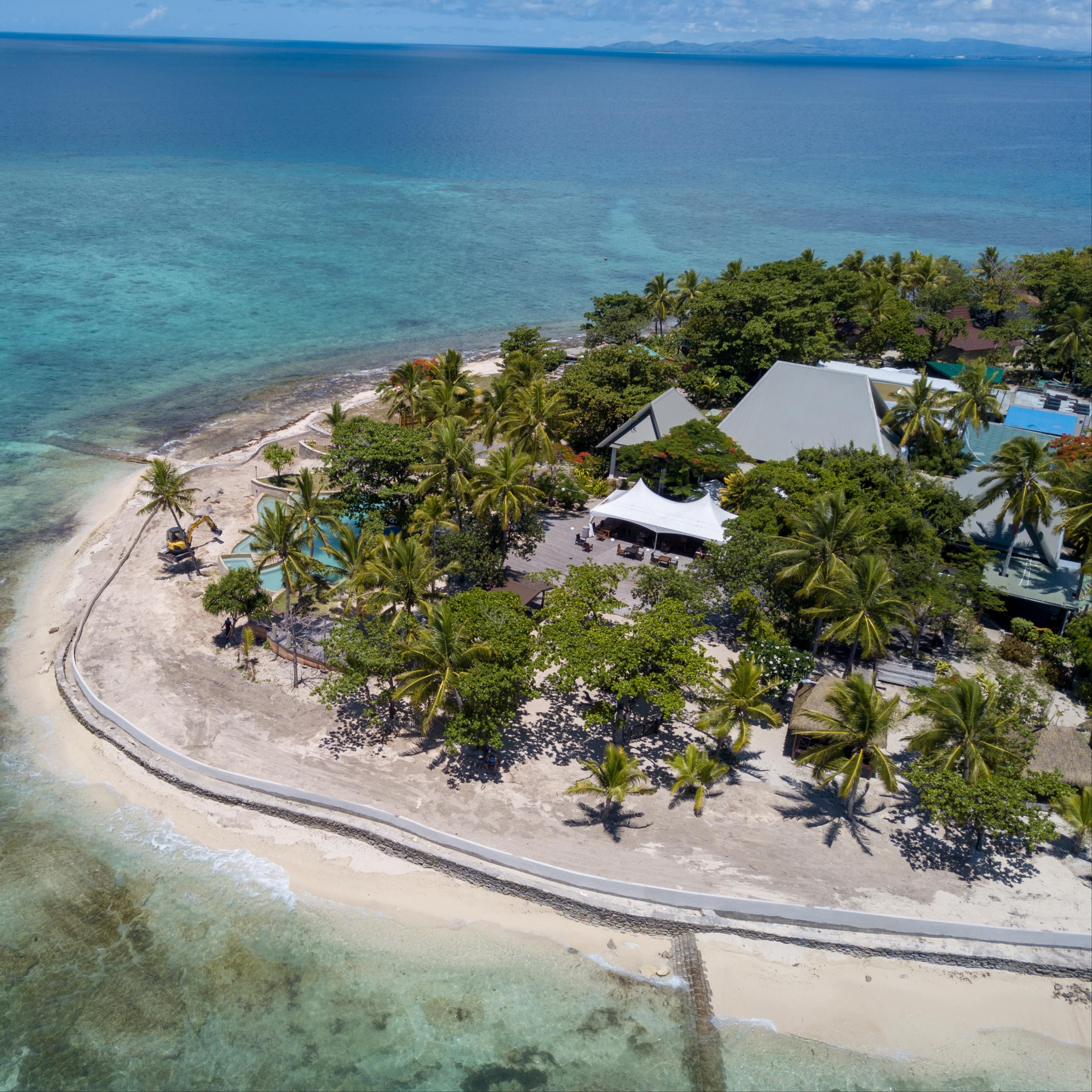 Villas set amongst tropical trees on a Fiji island with clear waters and reefs