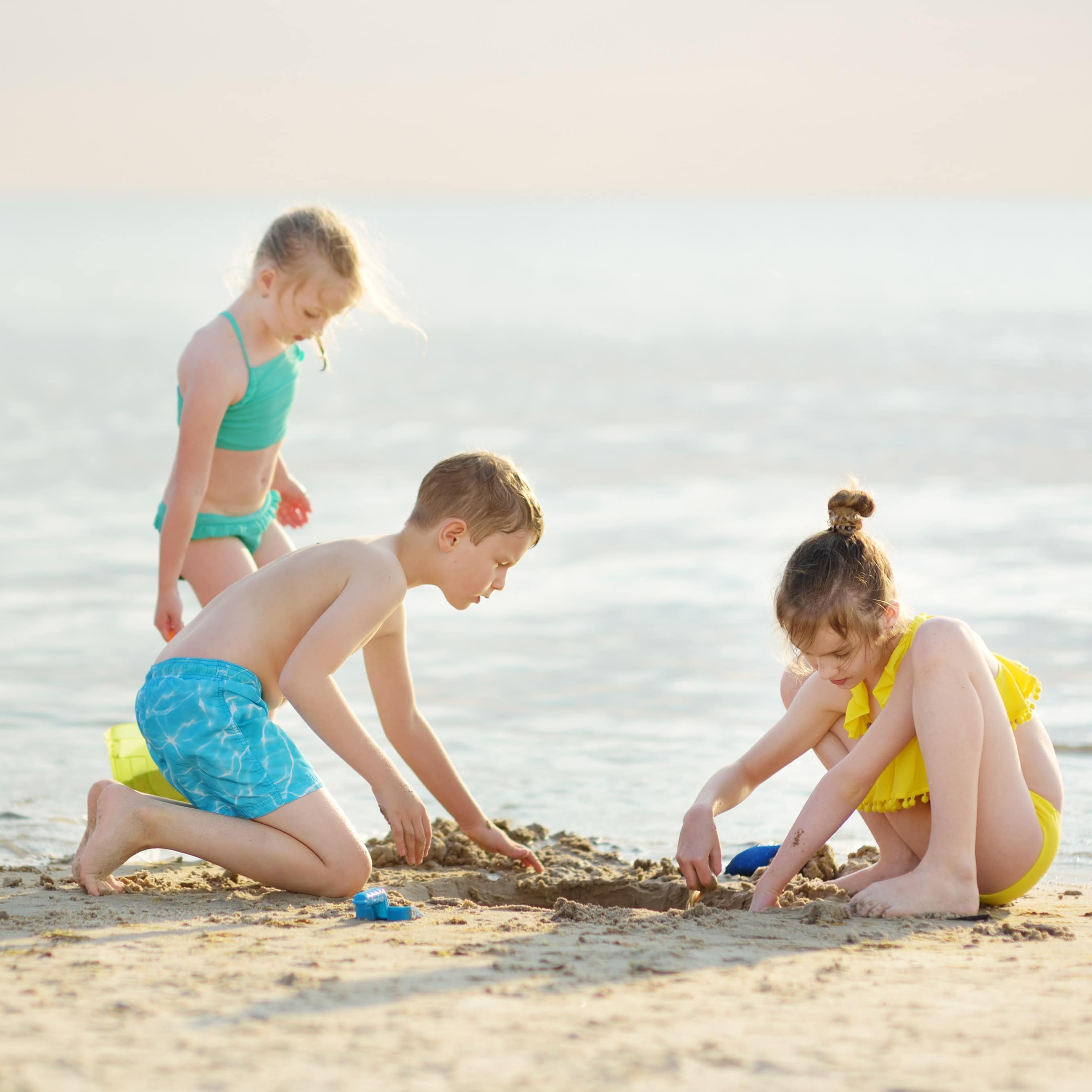 Siblings playing in the sand by the ocean