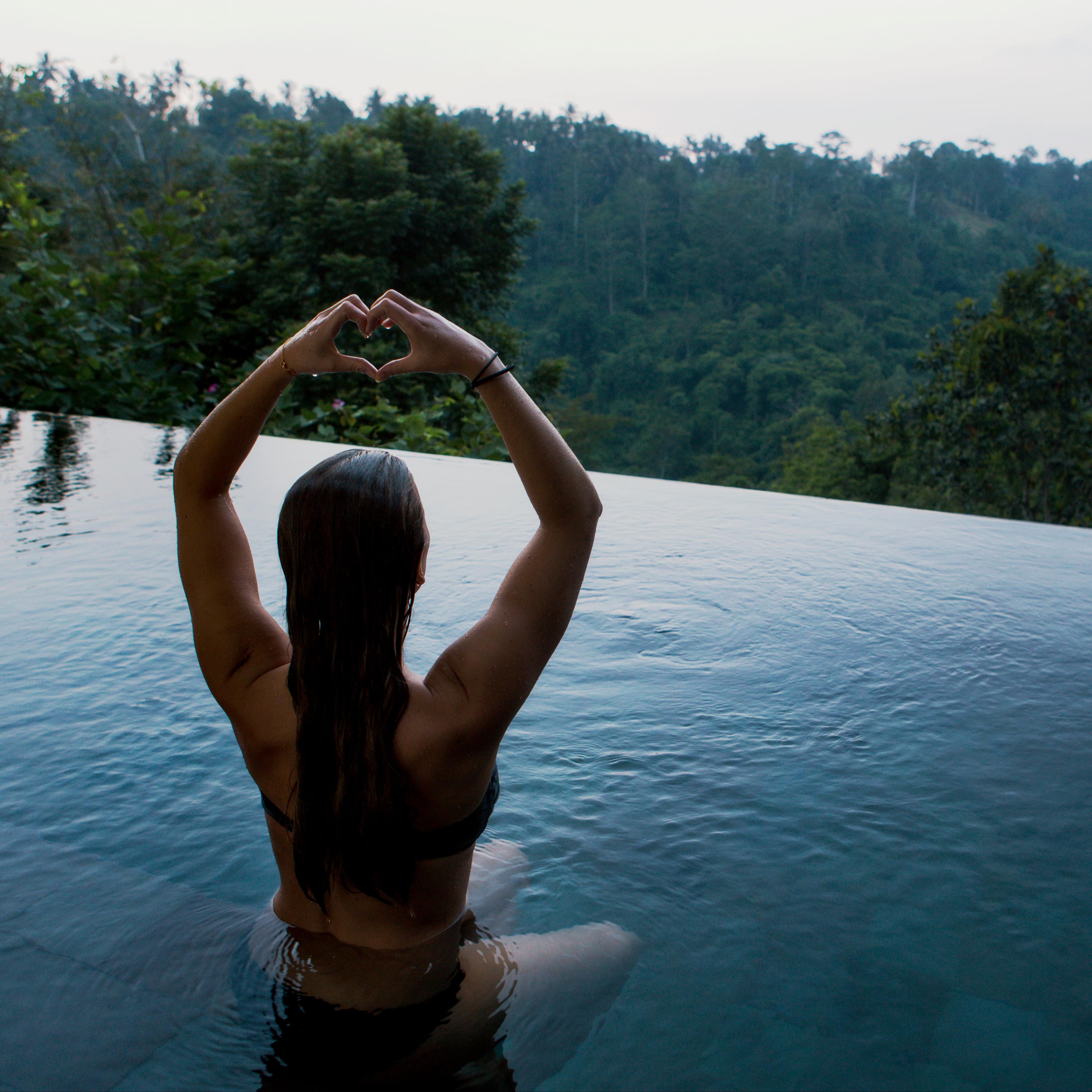 Woman meditating in a private infinity pool at Bali villa overlooking the tropical rainforest