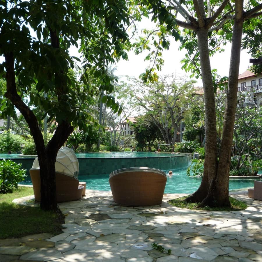 Two-level swimming pool with aqua-coloured tile, water spilling of the top level and wicker chairs under trees