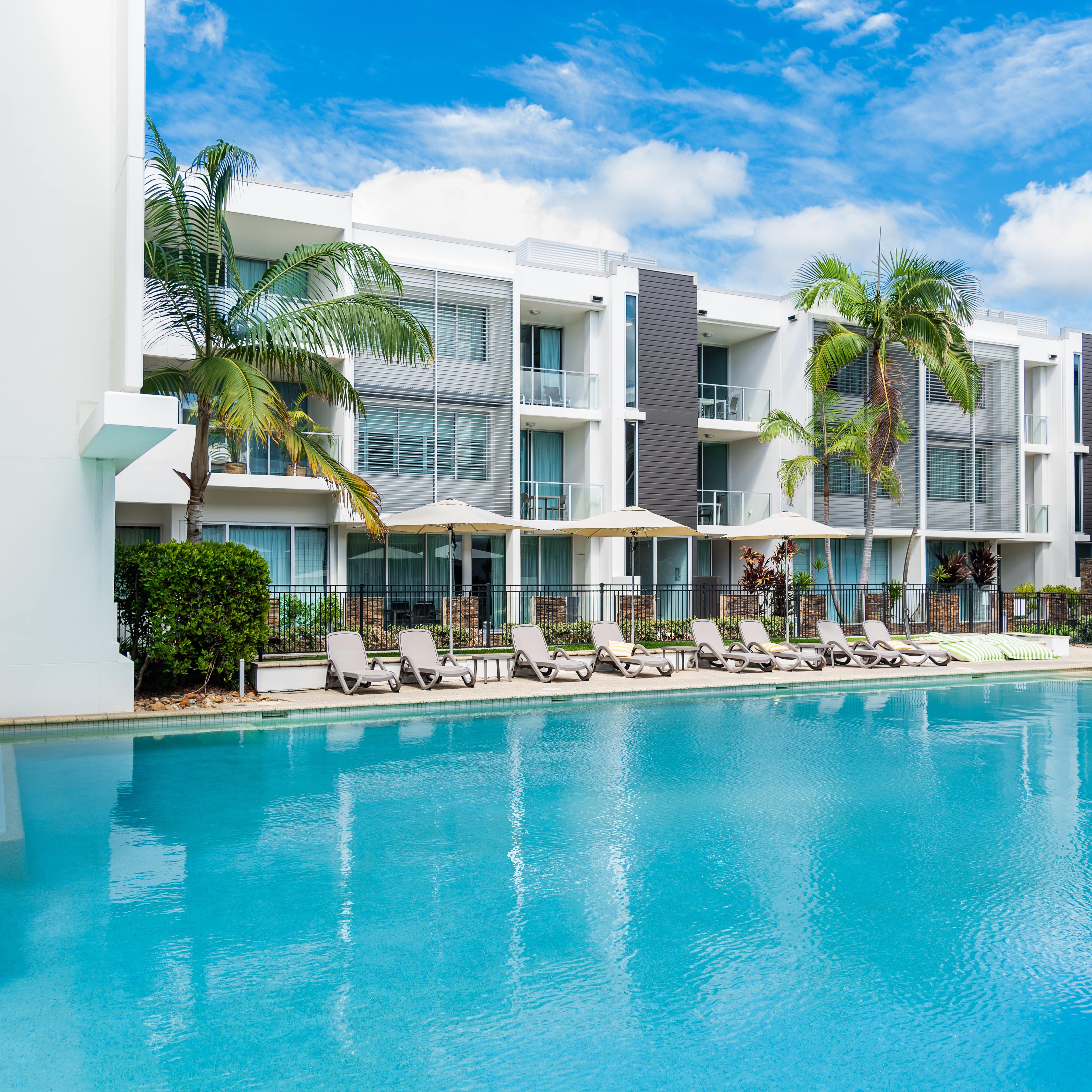 3-storey beachfront apartment with large, aquamarine pool and lounge area with chairs, shade umbrellas and palm trees