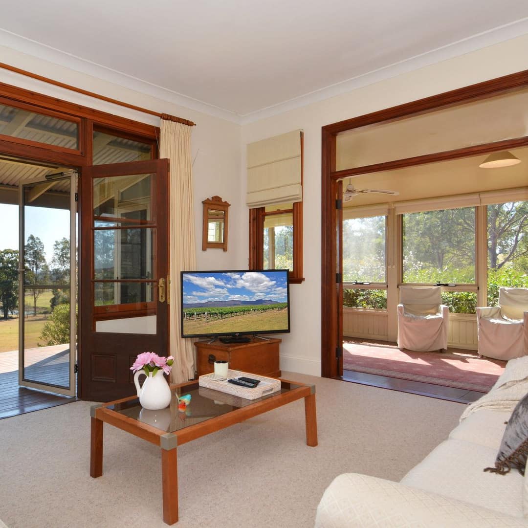 Open living room with white sofas and a television, attached sunroom, and open glass doors show views of a nearby vineyard.