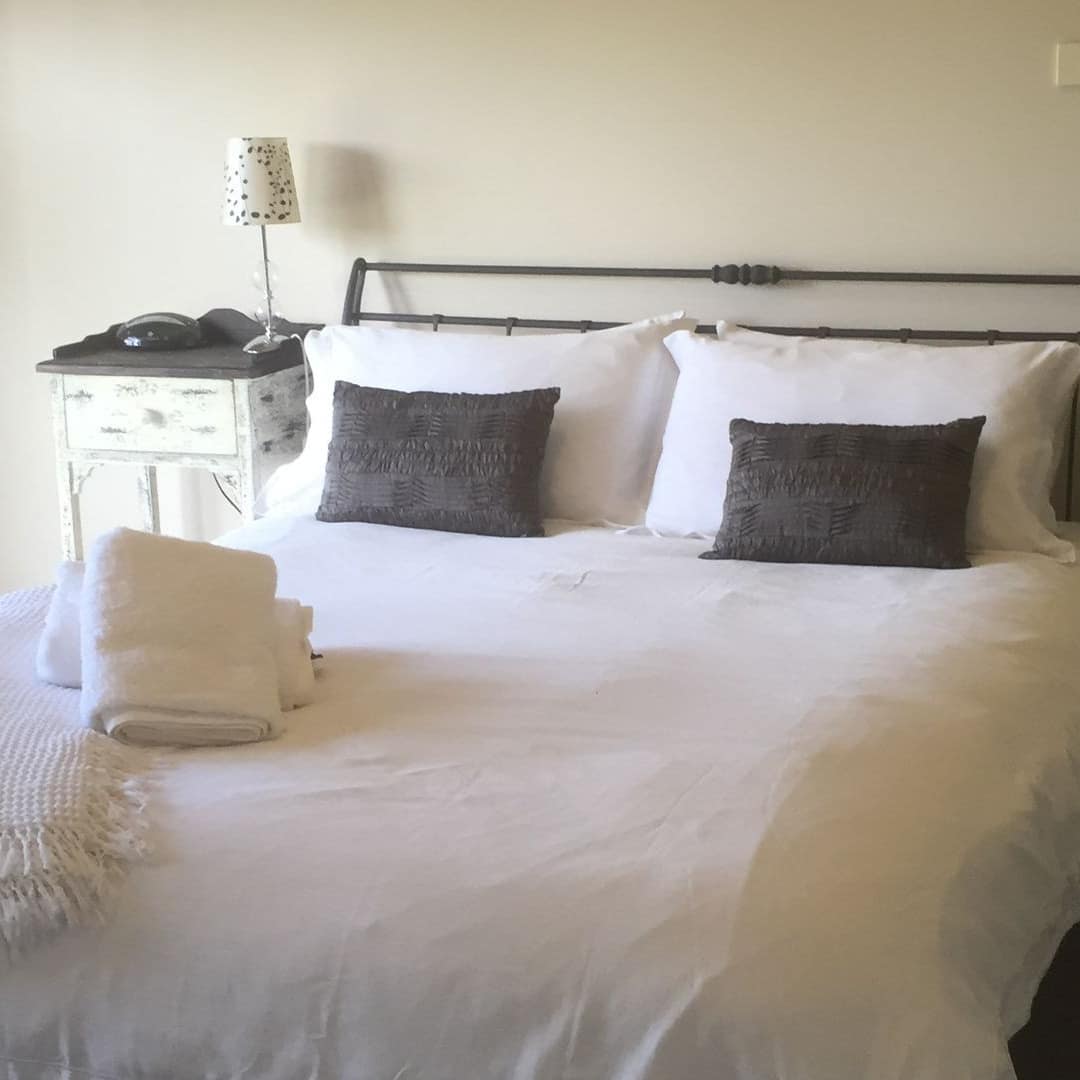 Neutral-toned bedroom with black metal king size bed, white bedding, white vintage bedside tables.