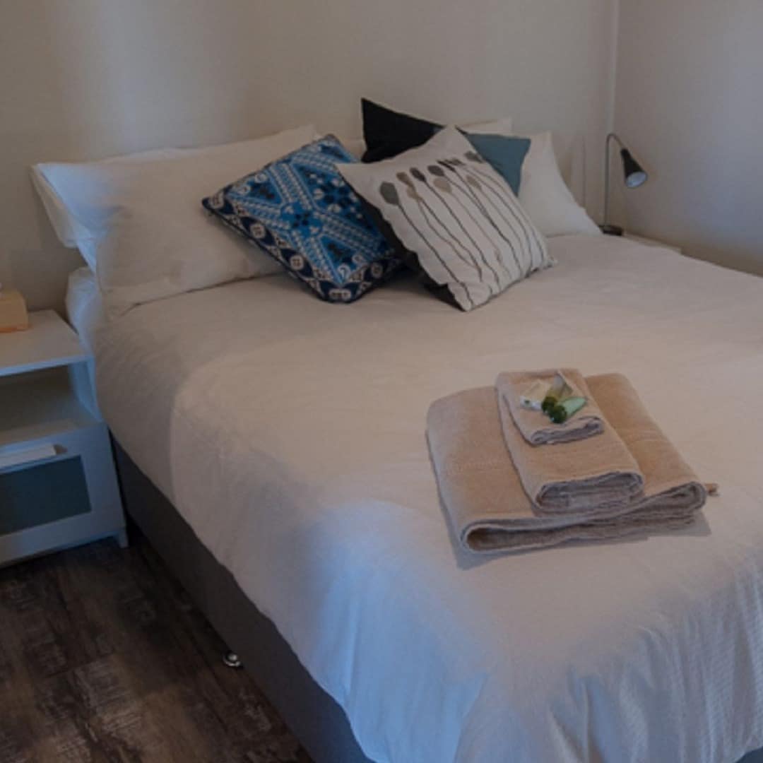 Bedroom with a queen size bed, white linen and blue pillows, and tan towels folded on bed.