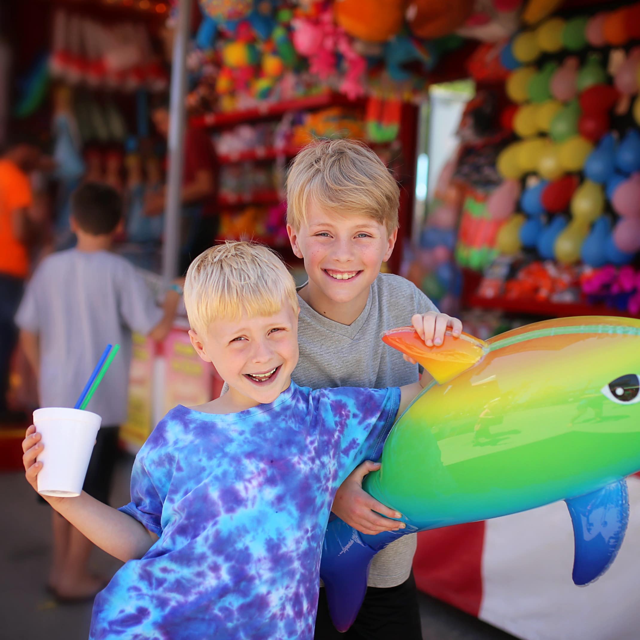 Two smiling boys win colorful dolphin prize at carnival game