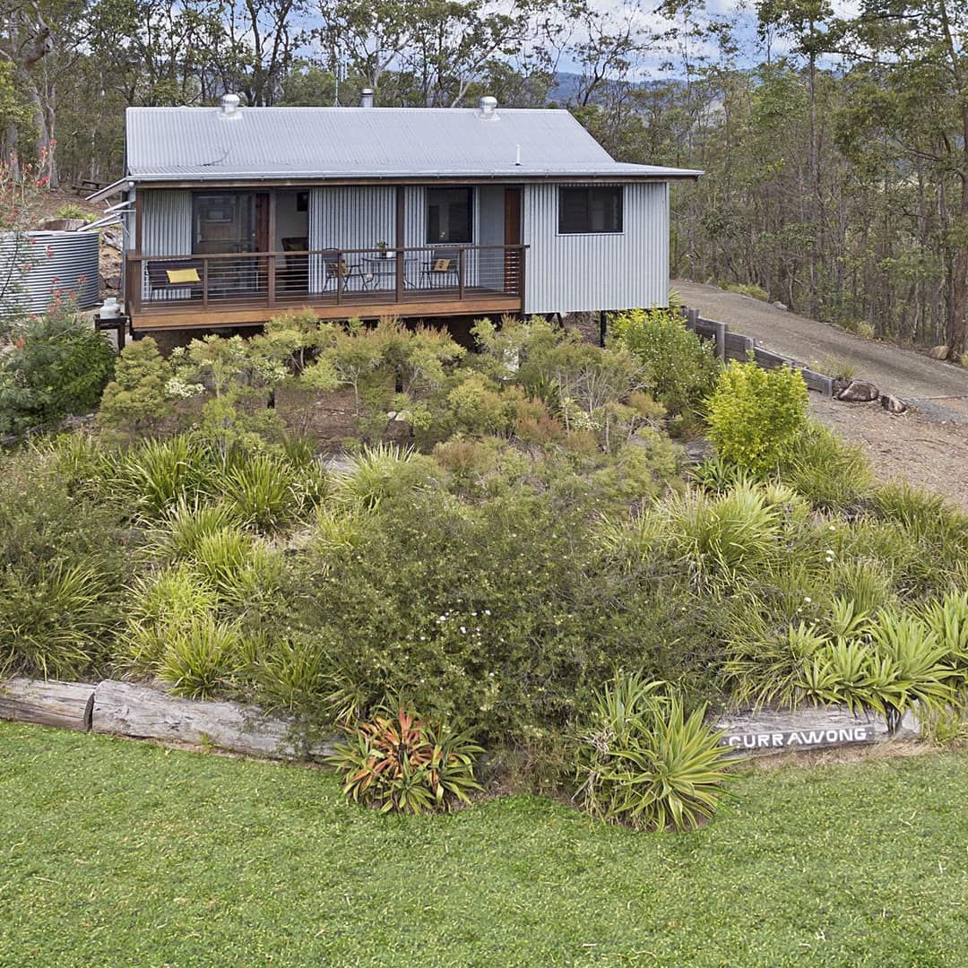 A grey cabin sitting atop a hill lined with green bushes