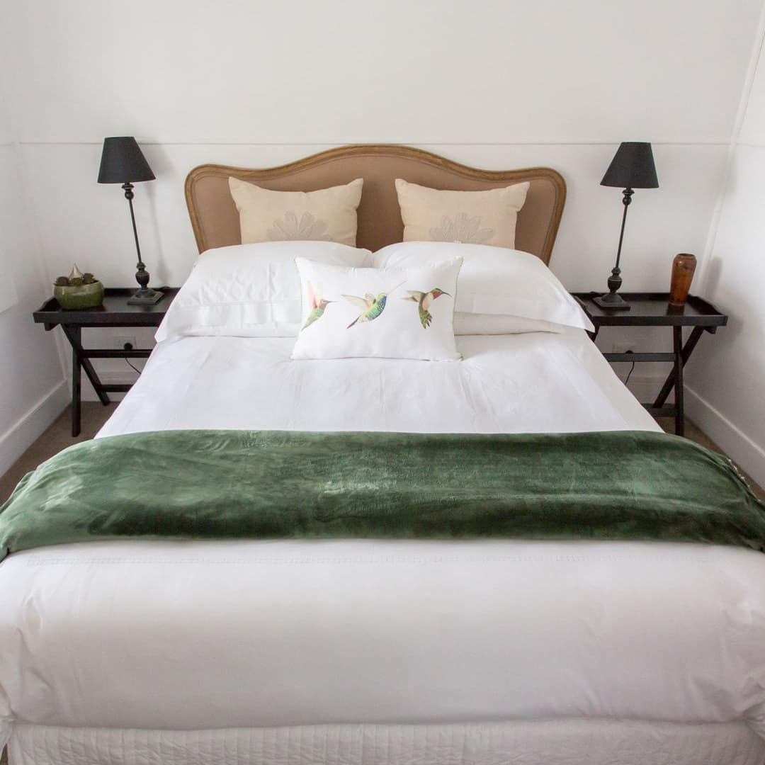 Bedroom with grey carpet and white walls, a queen size bed, white bedding, green blanket and matching black bedside tables.