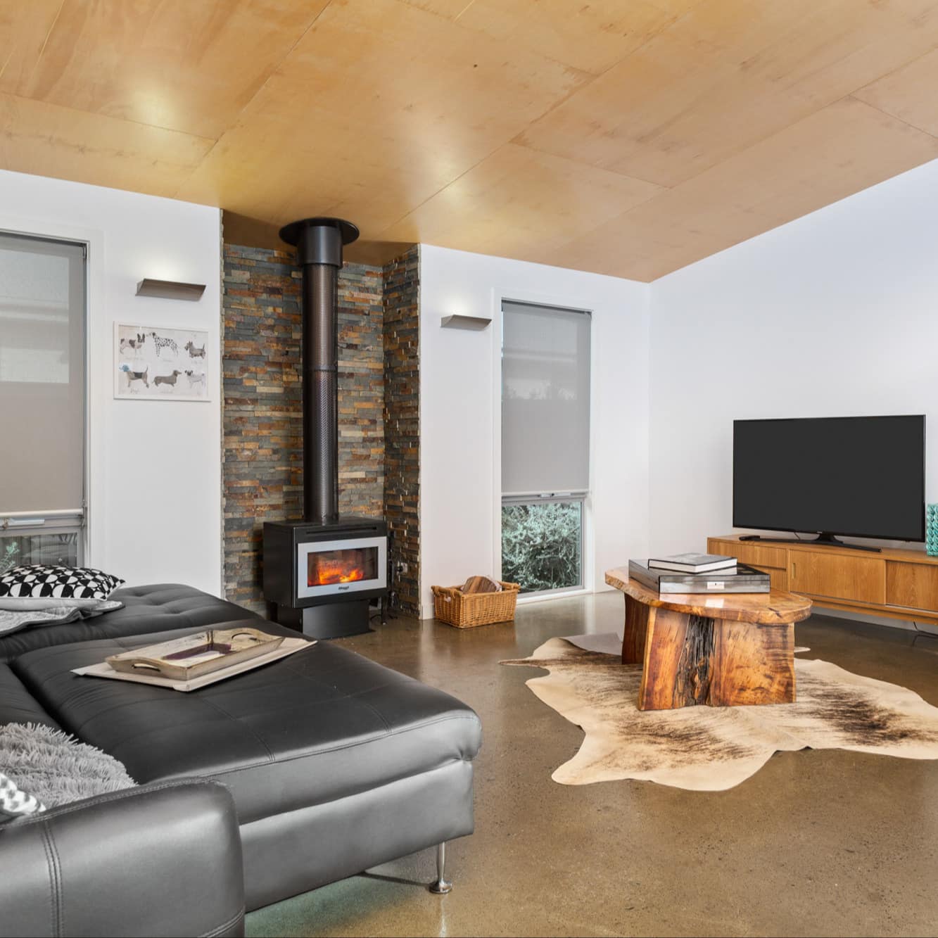 Spacious modern living room with leather sofa, beige chair, natural wood table, fireplace, and a flat-screen TV.