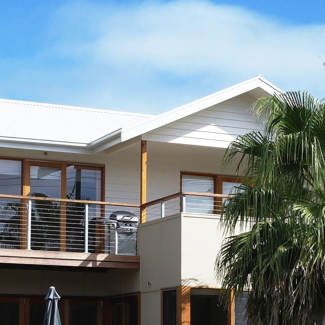 Two-storey white home with wood trim, second-storey balcony and ground floor patio space, palm trees.