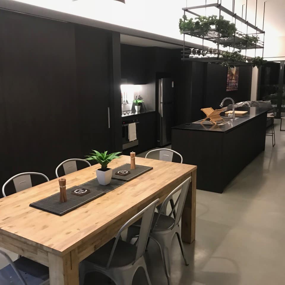 Modern, open kitchen and dining room, grey cement floor, black kitchen cabinets, wood dining table and metal chairs.