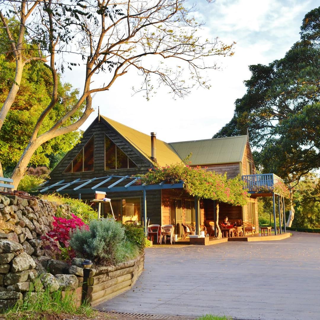 2-storey cabin near Kiama Blowhole with porch arbor covered with flowering vines, rock-walled garden and towering trees
