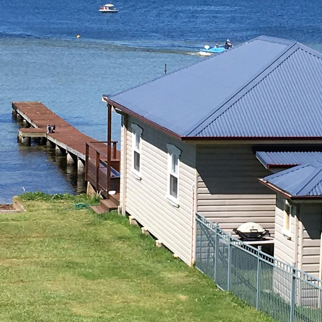 1-bedroom, grey beach cabin with blue metal roof, fenced yard and wood dock stretching over the water