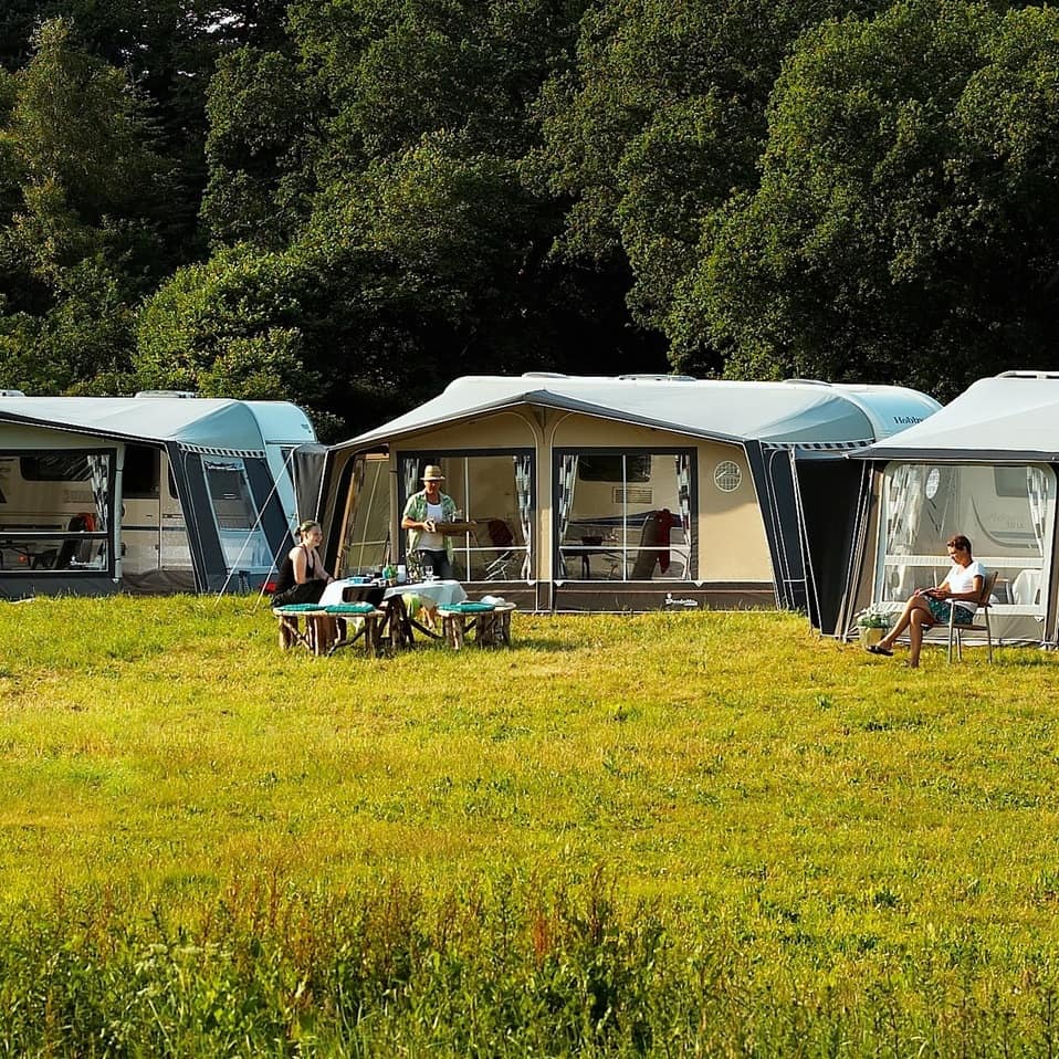 Three glamping tents in the middle of a meadow with people reading and eating outdoors
