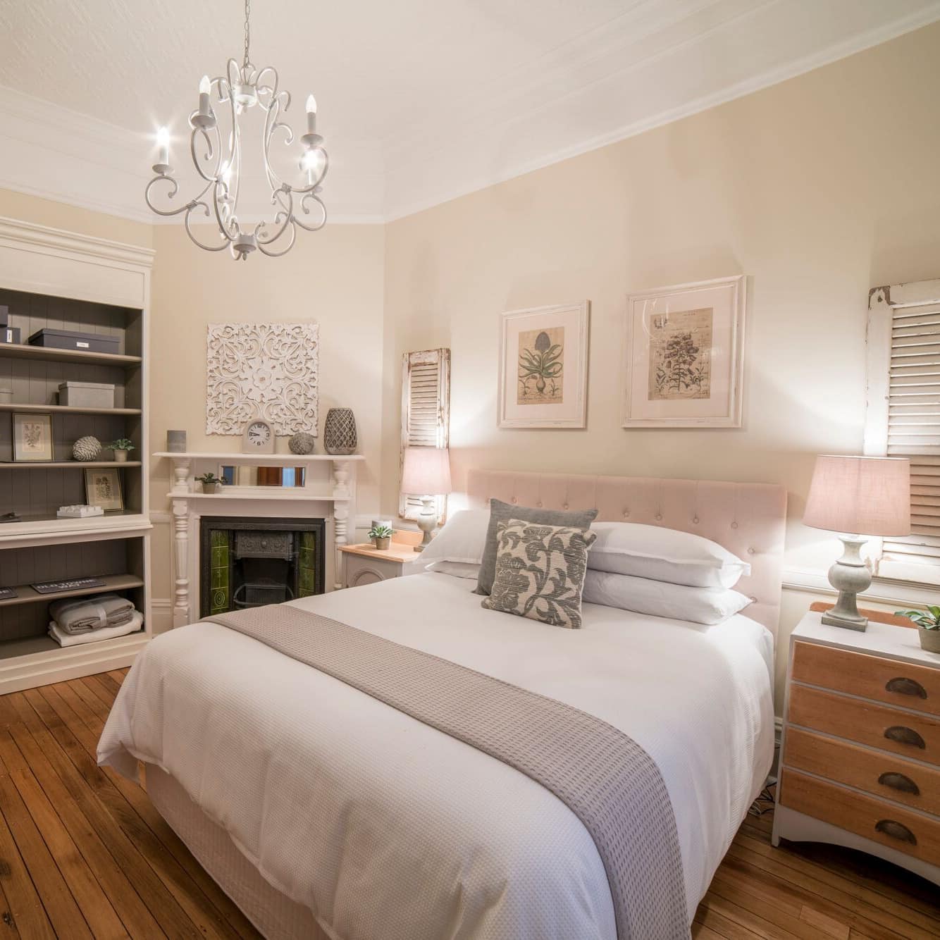 Charming bedroom, hardwood floors, king-size bed with pink bed frame, white and grey bedding, fireplace, vintage art.