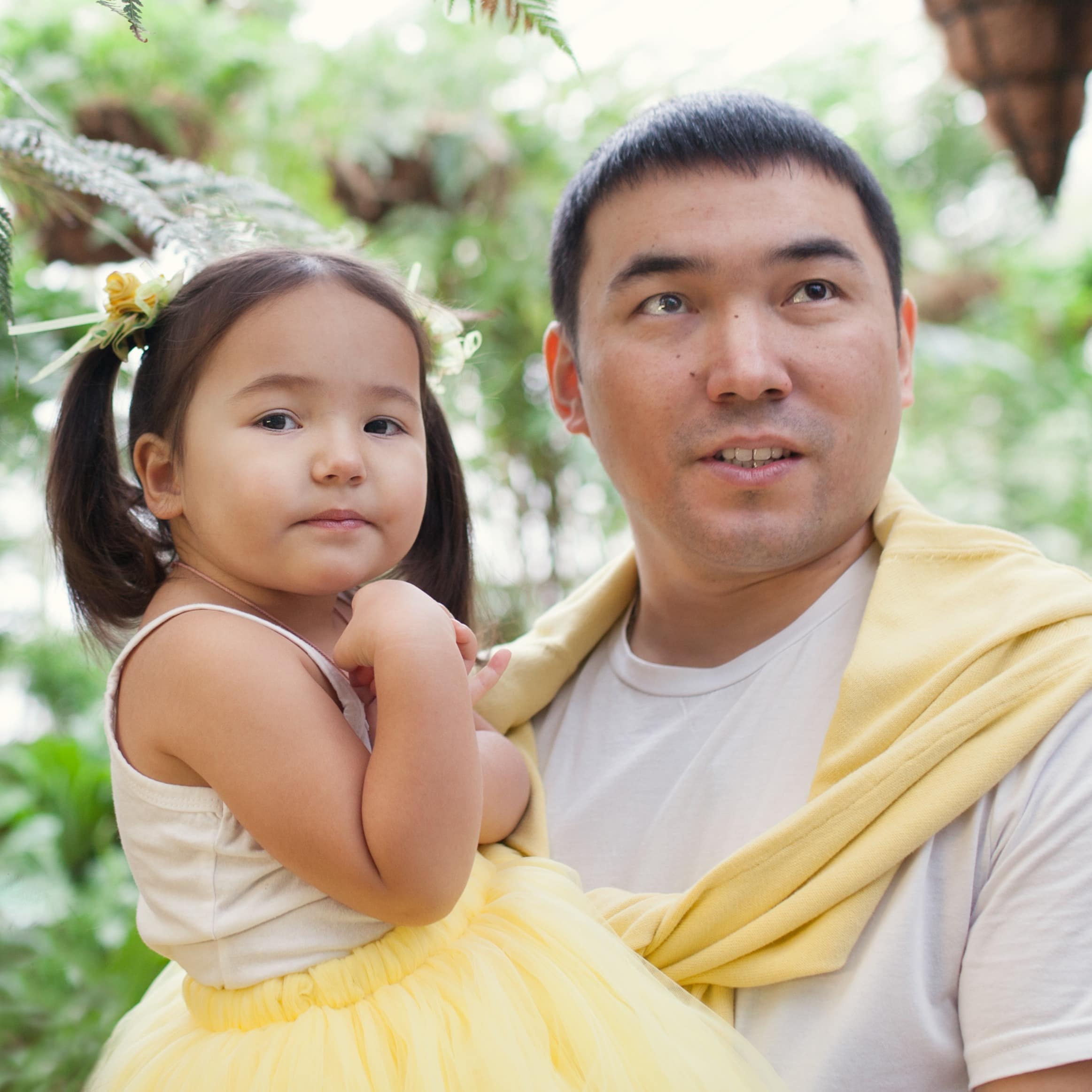 Portrait of a father and little daughter dressed in yellow and white in a botanical garden