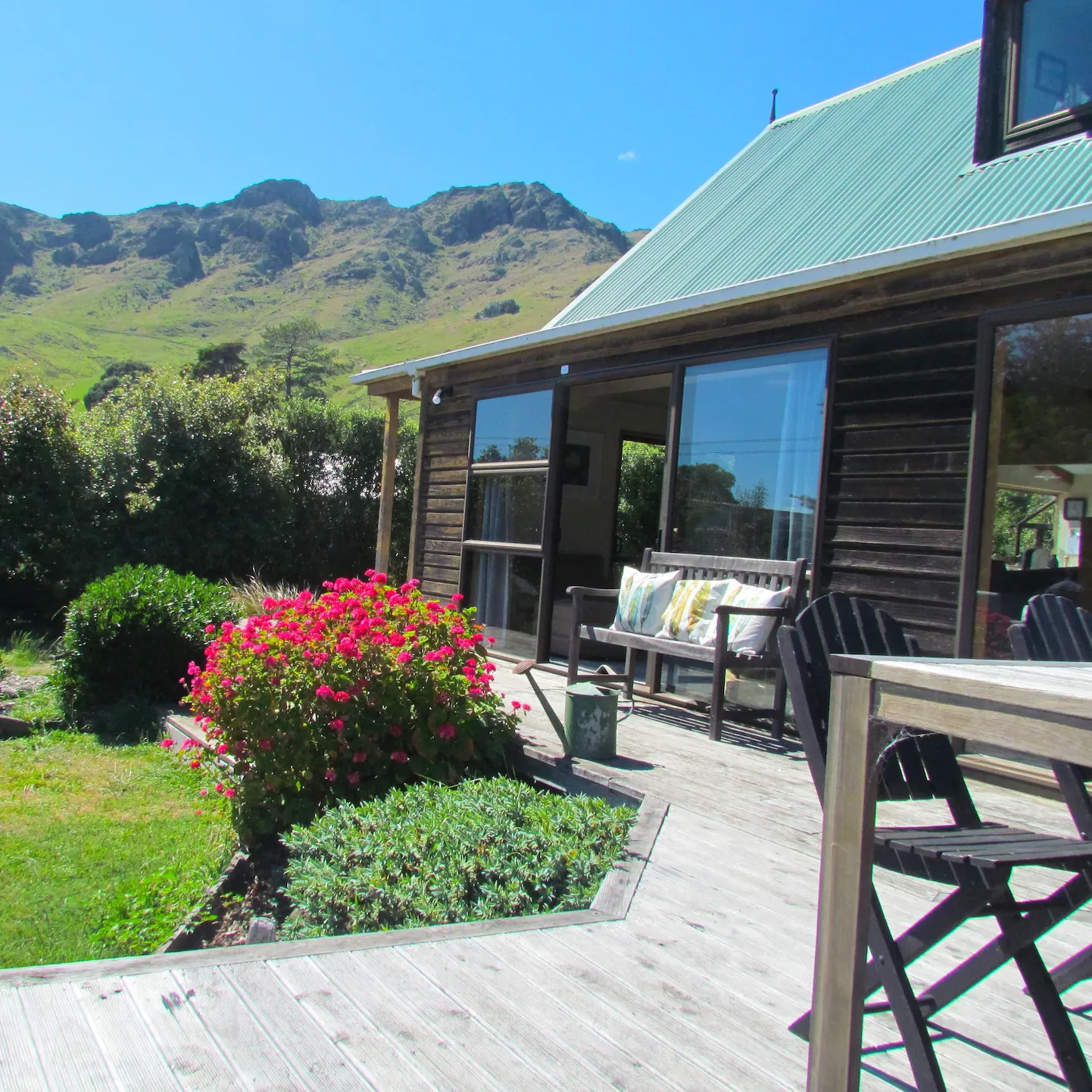 A lodge in Christchurch with the deck and a pink flower bush in the foreground with green hills in the distance 