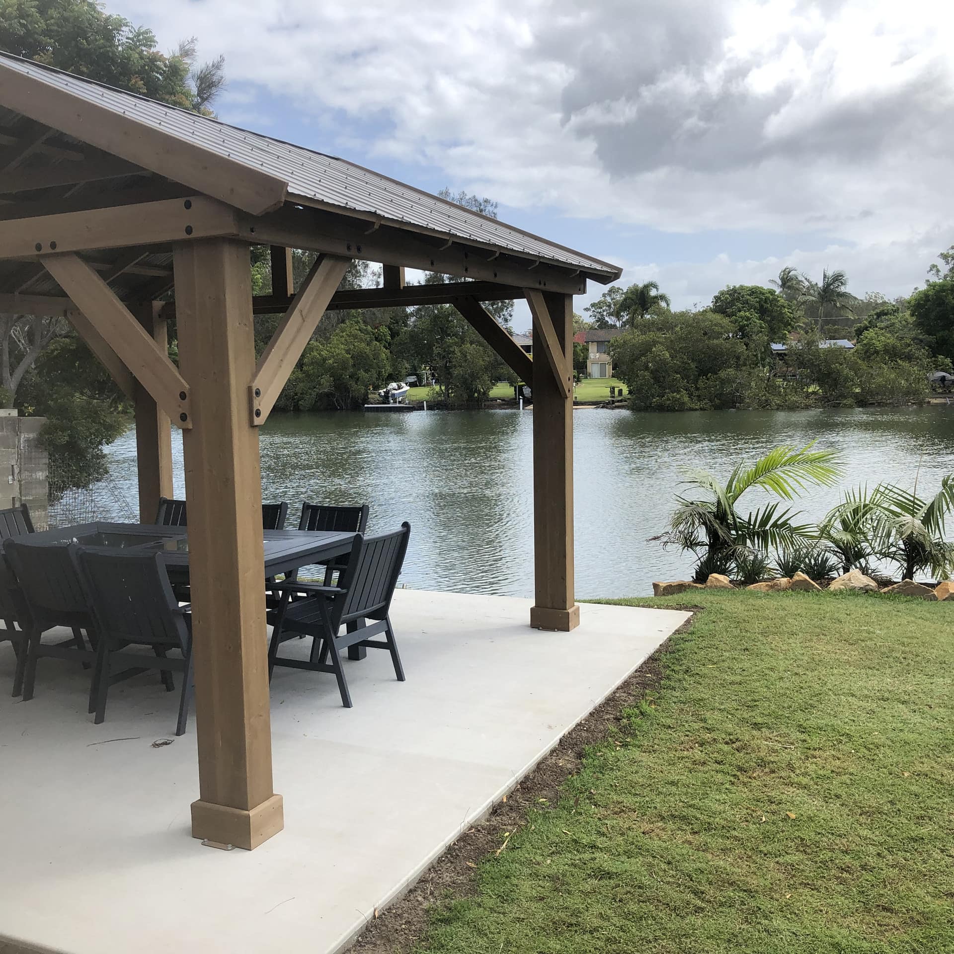 A pergola with outdoor dining on a prominence by the Kalang River with wind-swept waters and sun peeking through clouds.