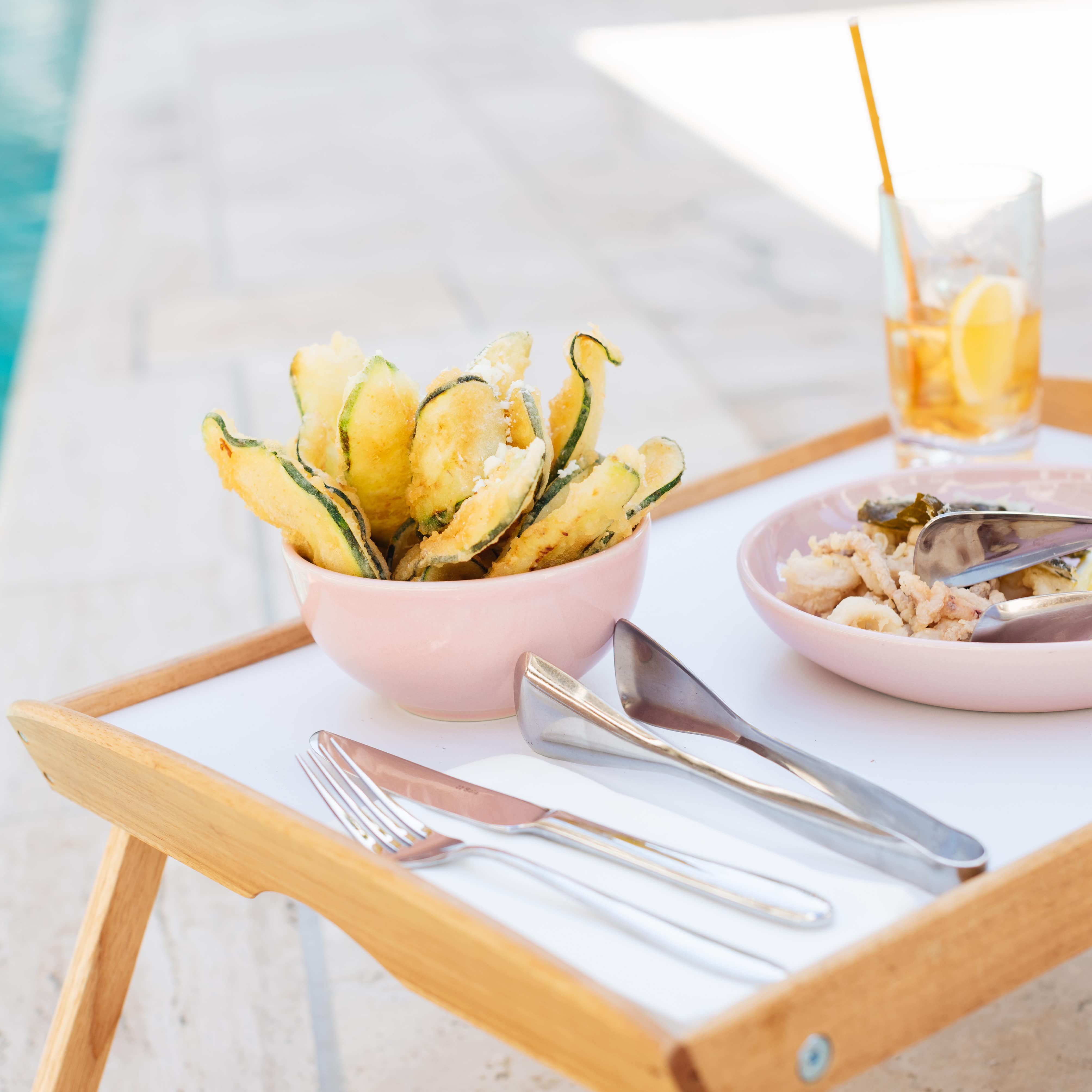 Lunch by the pool at a Brisbane apartment with a dinner tray, fried zucchini, calamari and tea on a patio by sparkling water
