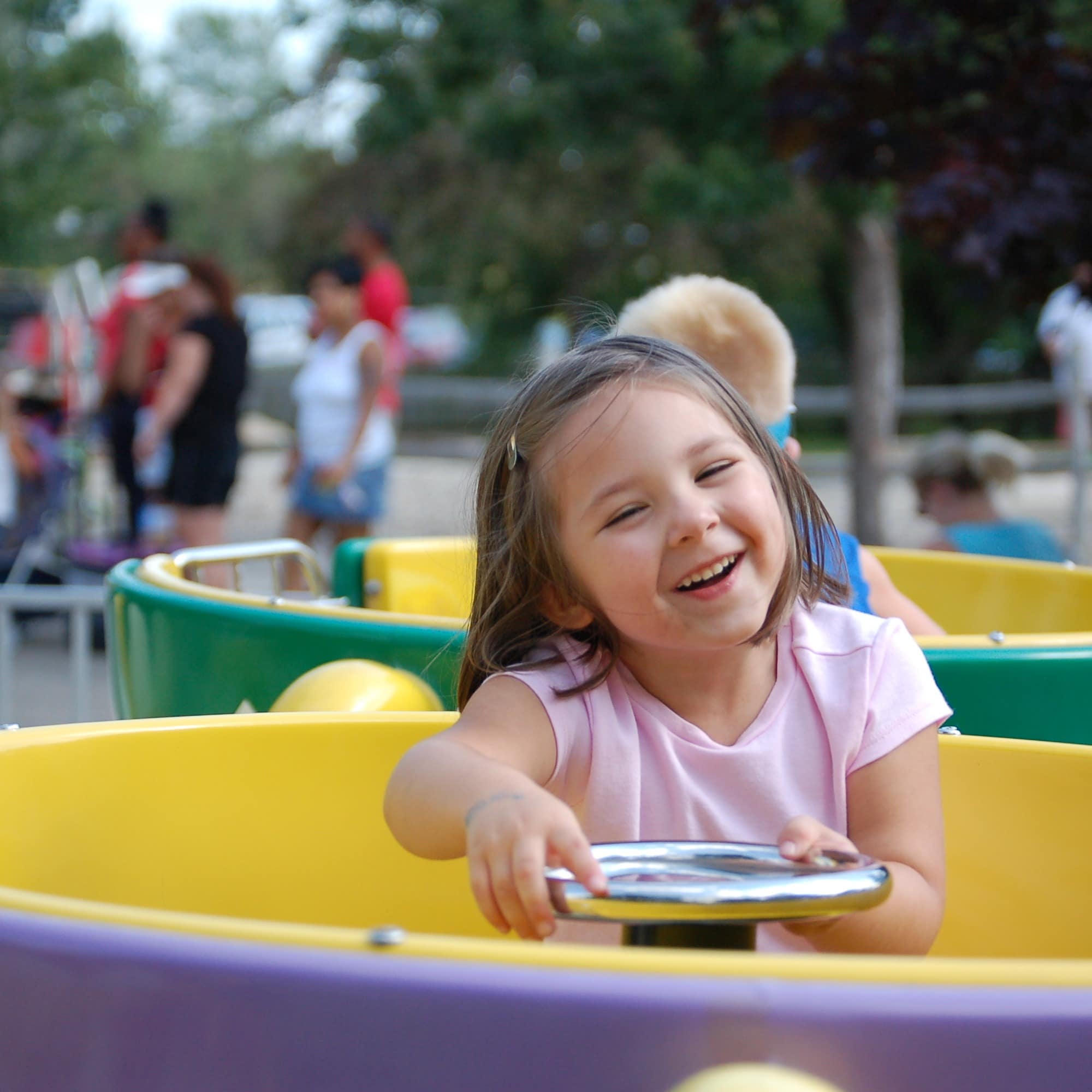 Smiling little girl riding in tea cup at amusement park