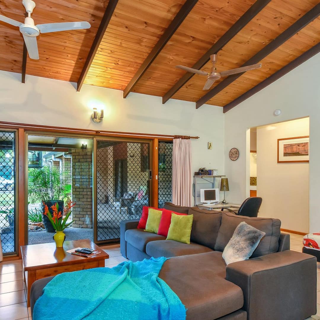 Open living room with high, vaulted ceiling, colourful decor, grey L-shaped sectional, glass doors open onto the patio.