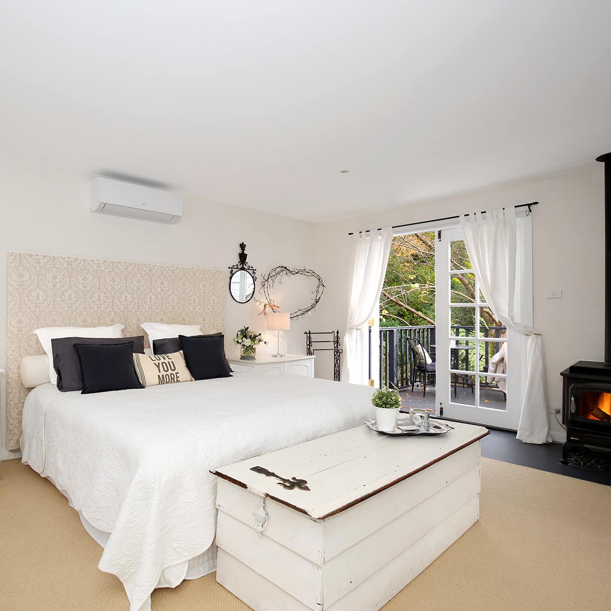 Spacious bedroom with a king-size bed, white and black bedding, white trunk, gas fireplace, and vintage decor.