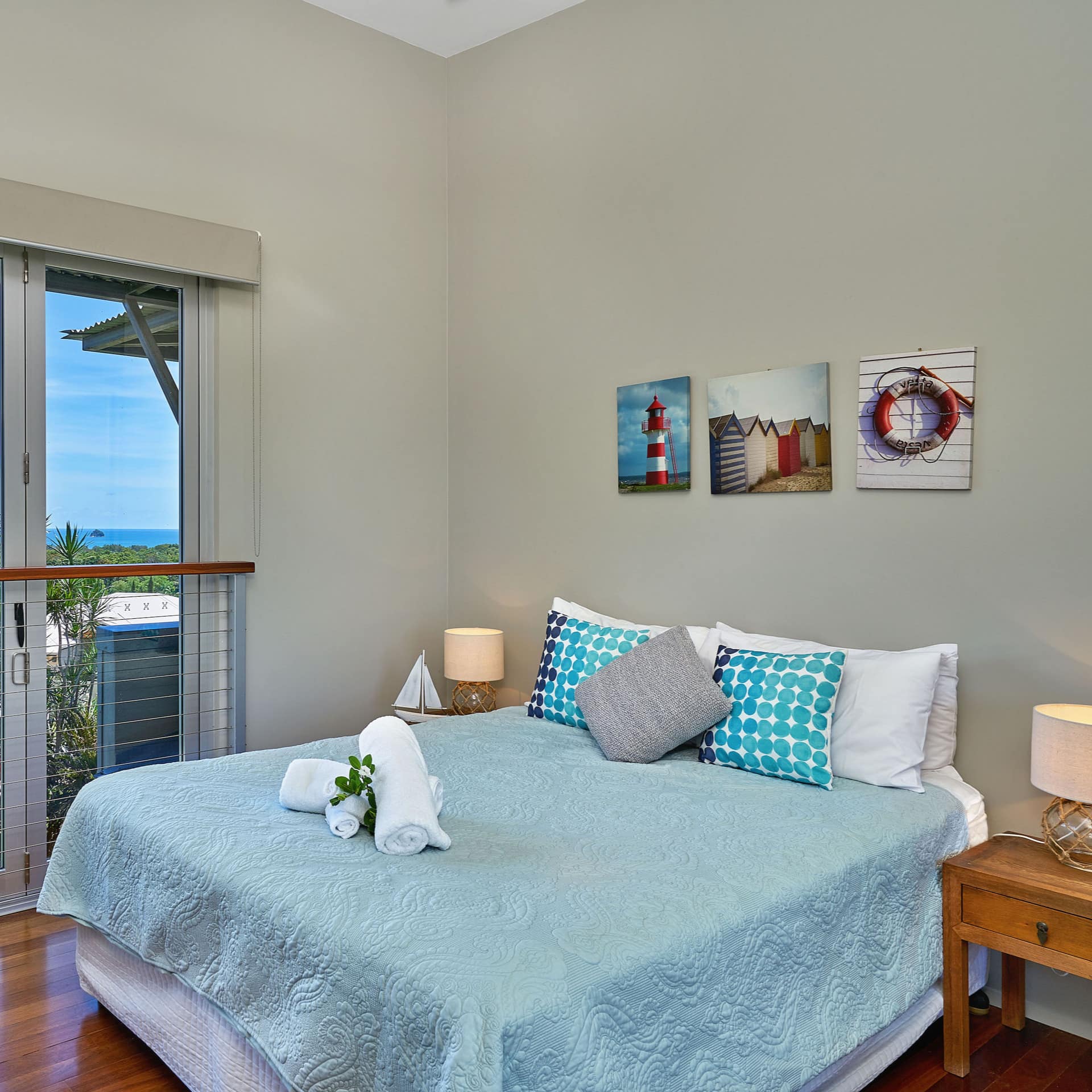 Bedroom with hardwood floors, a king size bed, blue bedding, nautical art, tall windows with neighborhood and ocean views.