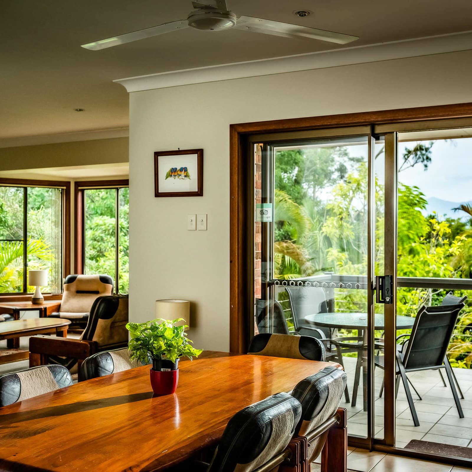 Open dining and living room with attached balcony, tan and black furnishings, and panoramic views of rainforest.
