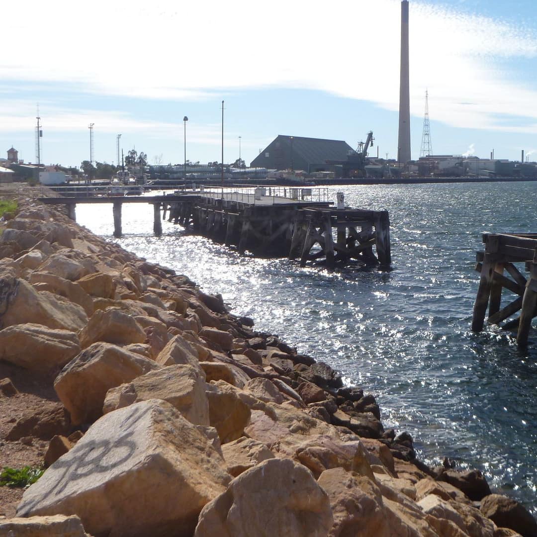 View of rocky sea wall and wooden pier in sparkling water.