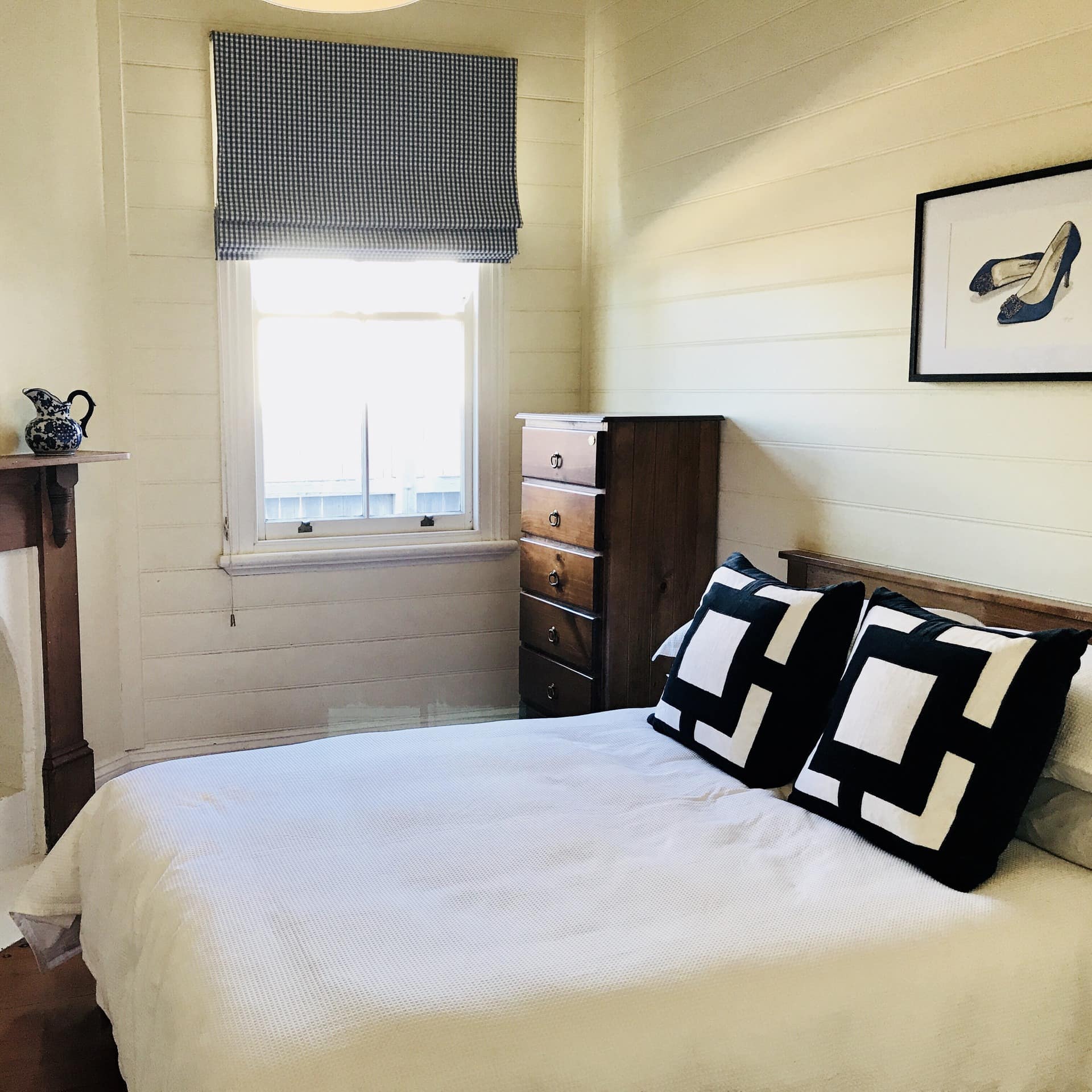 Rustic bedroom with white brick walls, hardwood floors, a queen size bed, white linen, and a fireplace with wood mantle.