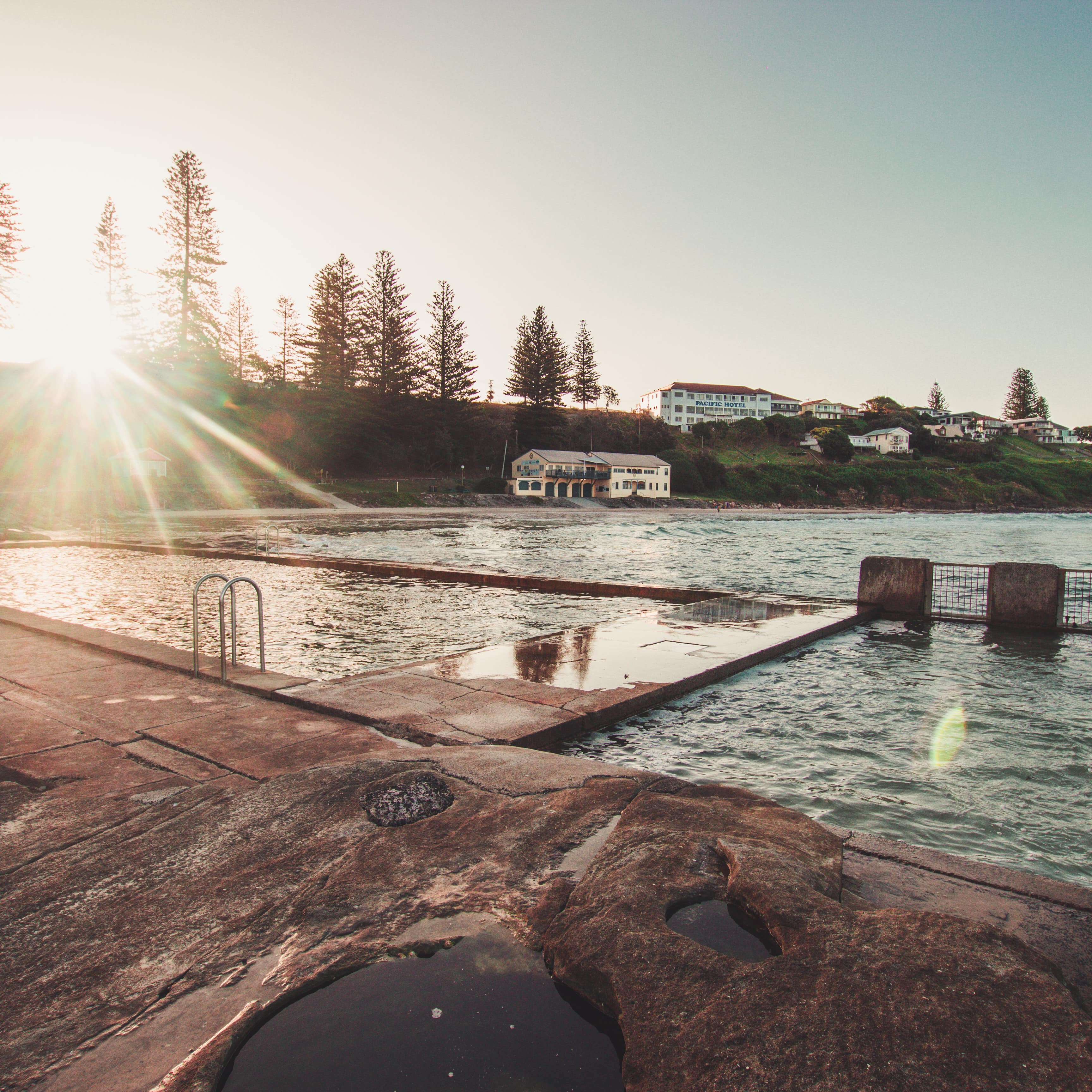 Iconic Yamba ocean pool surrounded by ocean, rock and shoreline hills with trees and houses