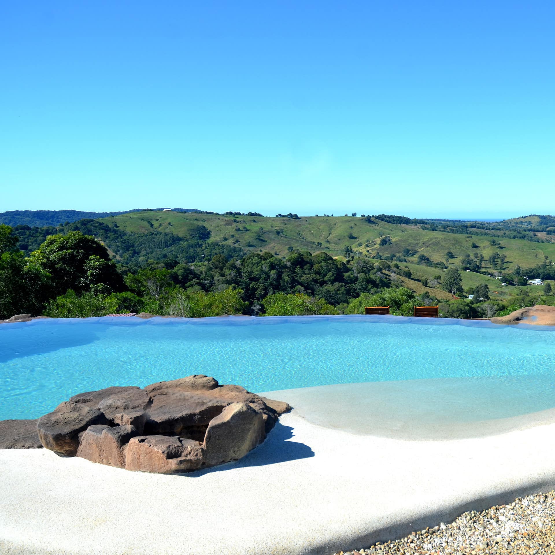 A sparkling blue inground pool encircled by pebble gravel and natural stones, with expansive views of rolling hills.