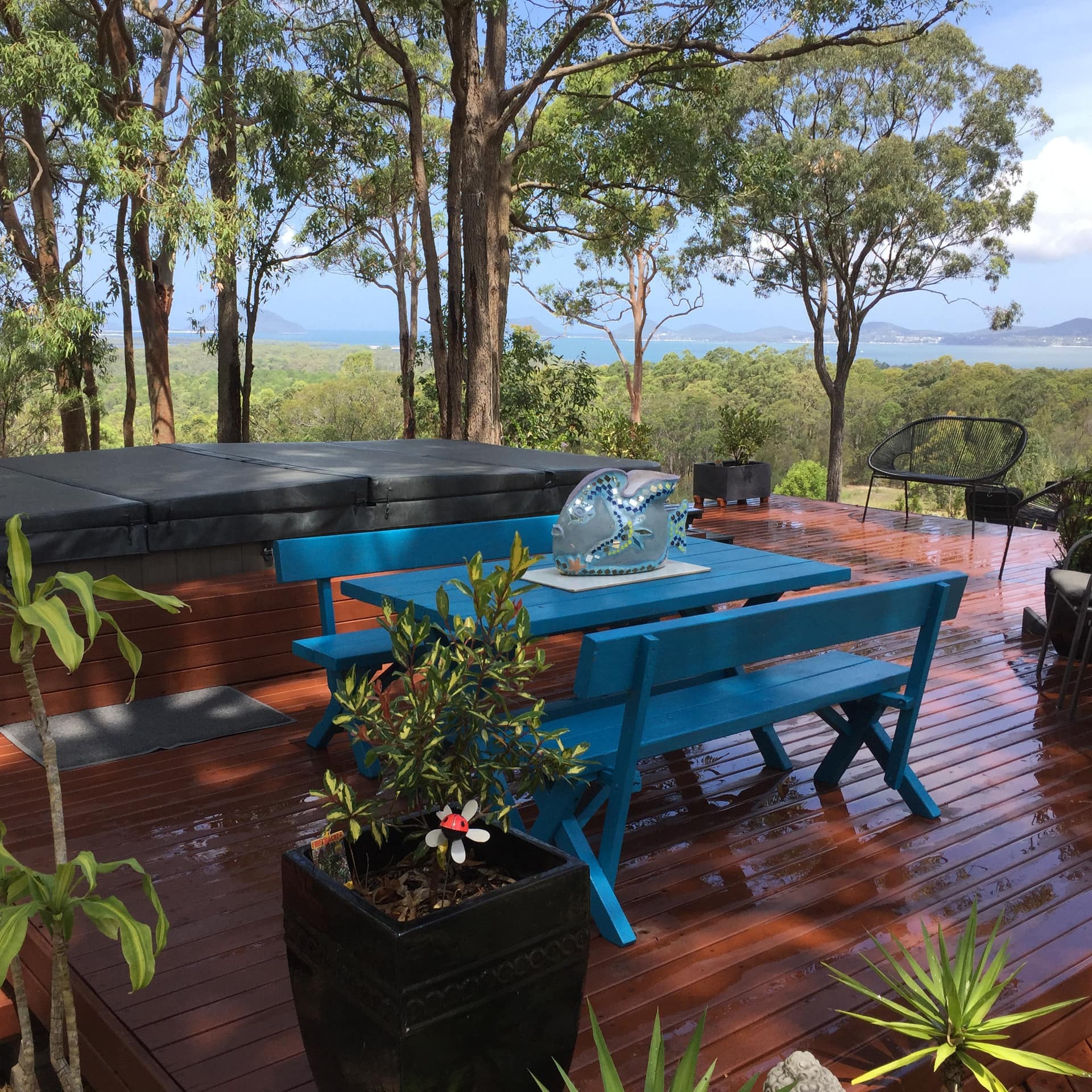 Deck with blue picnic table and jacuzzi with a view of trees, mountains, and water