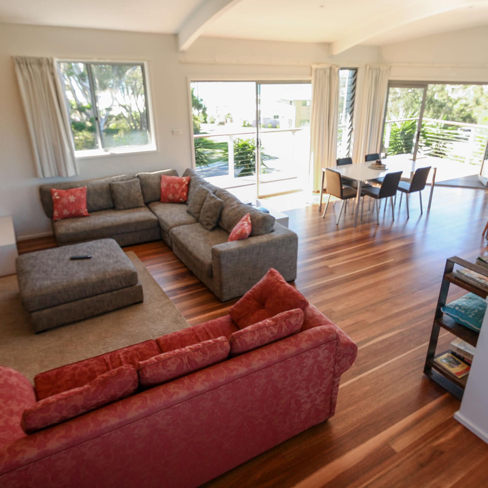 Open living and dining room with grey and red sofas, hardwood floors, and sliding glass doors that lead to a balcony.